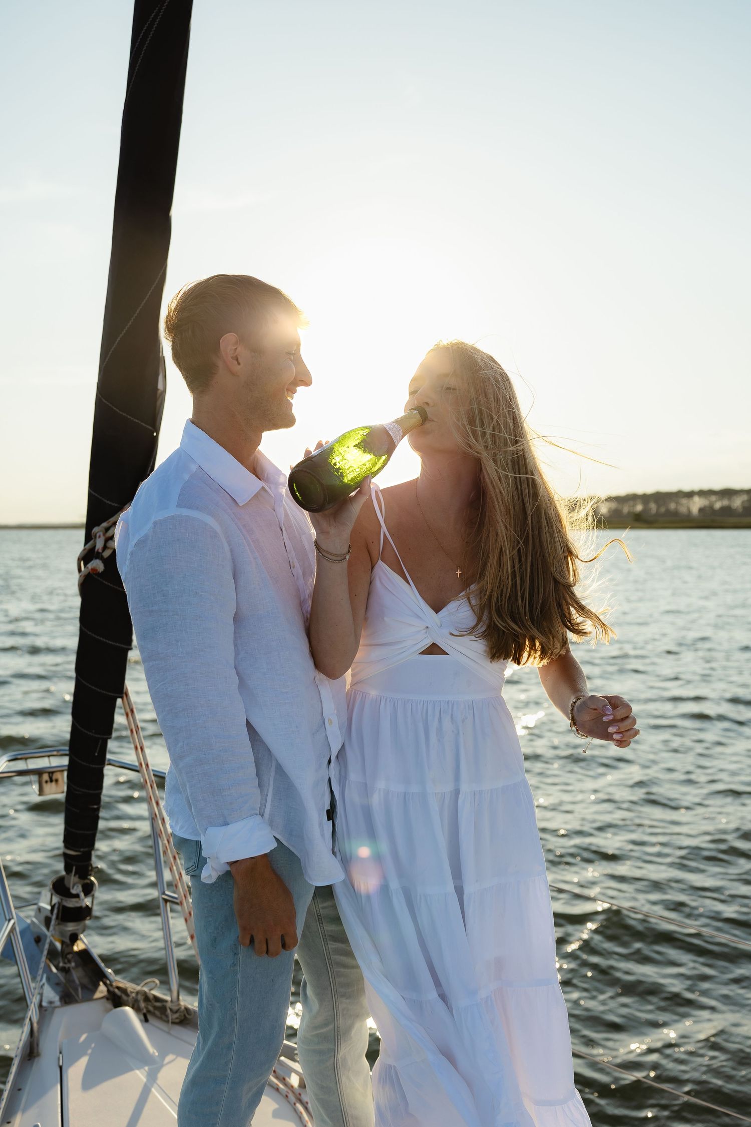 Romantic couple sharing champagne on sailboat at golden sunset over sparkling water.