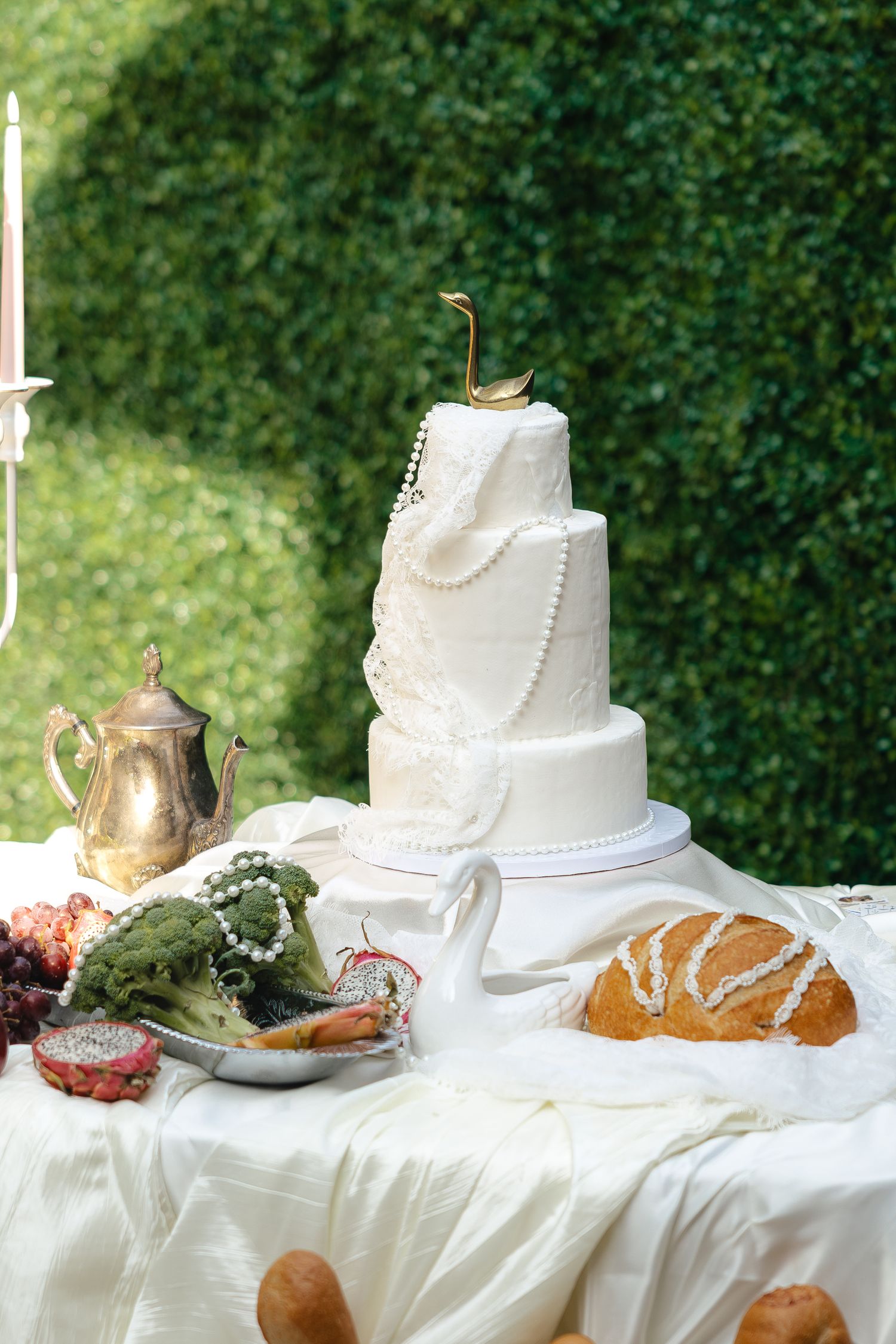 Elegant three-tier white wedding cake with pearl decorations and gold swan topper on a decorated table outdoors.