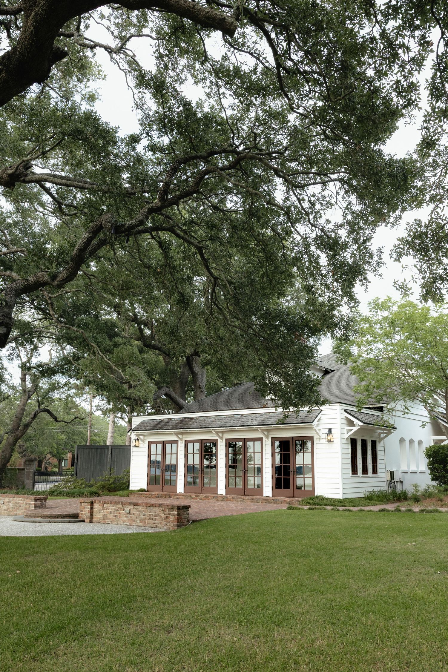 Charming white cottage with large oak tree canopy on a lush green lawn.