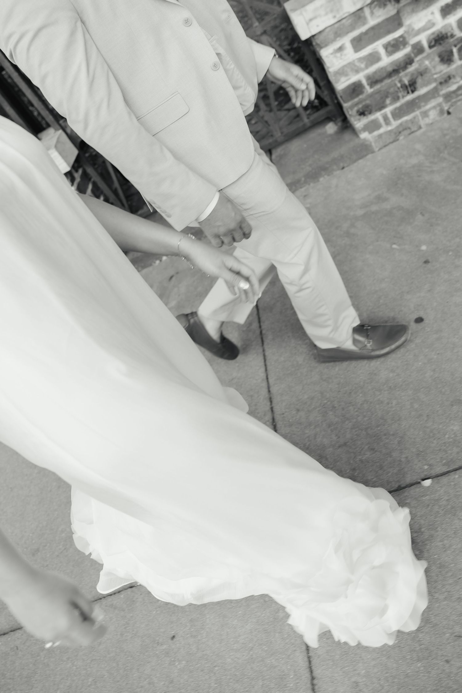 Black and white photo of bride and groom holding hands walking on a brick sidewalk.