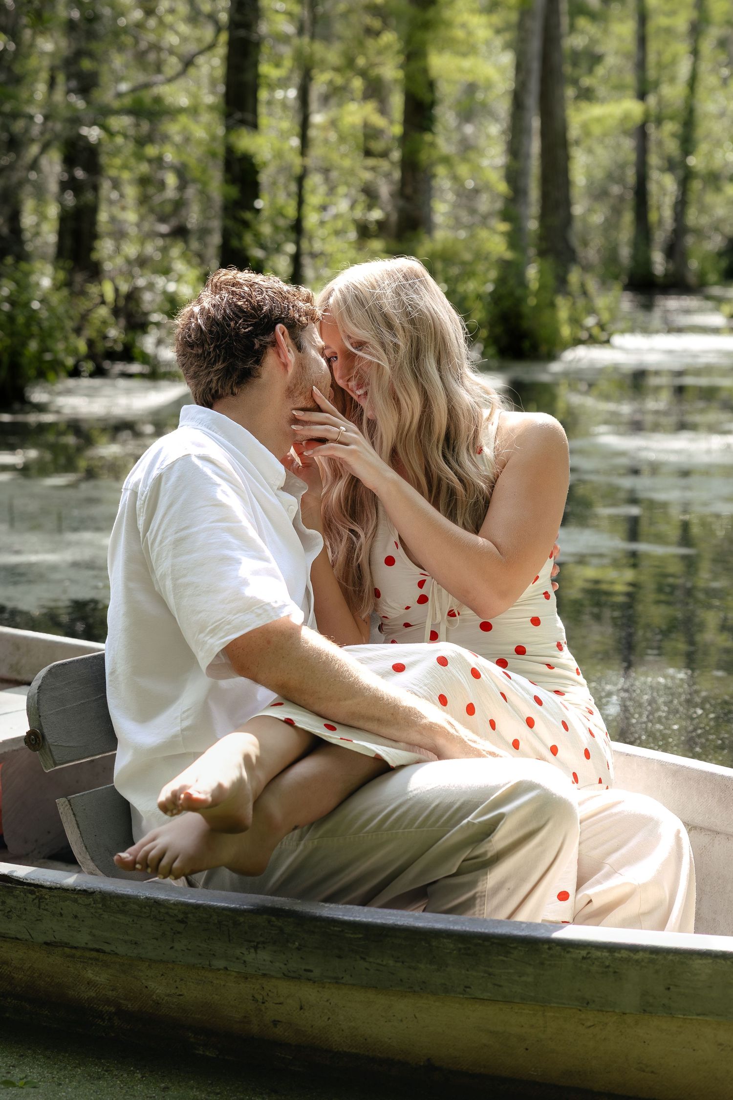Couple sharing an intimate moment in a rowboat on a tranquil swamp, woman in polka dot dress.