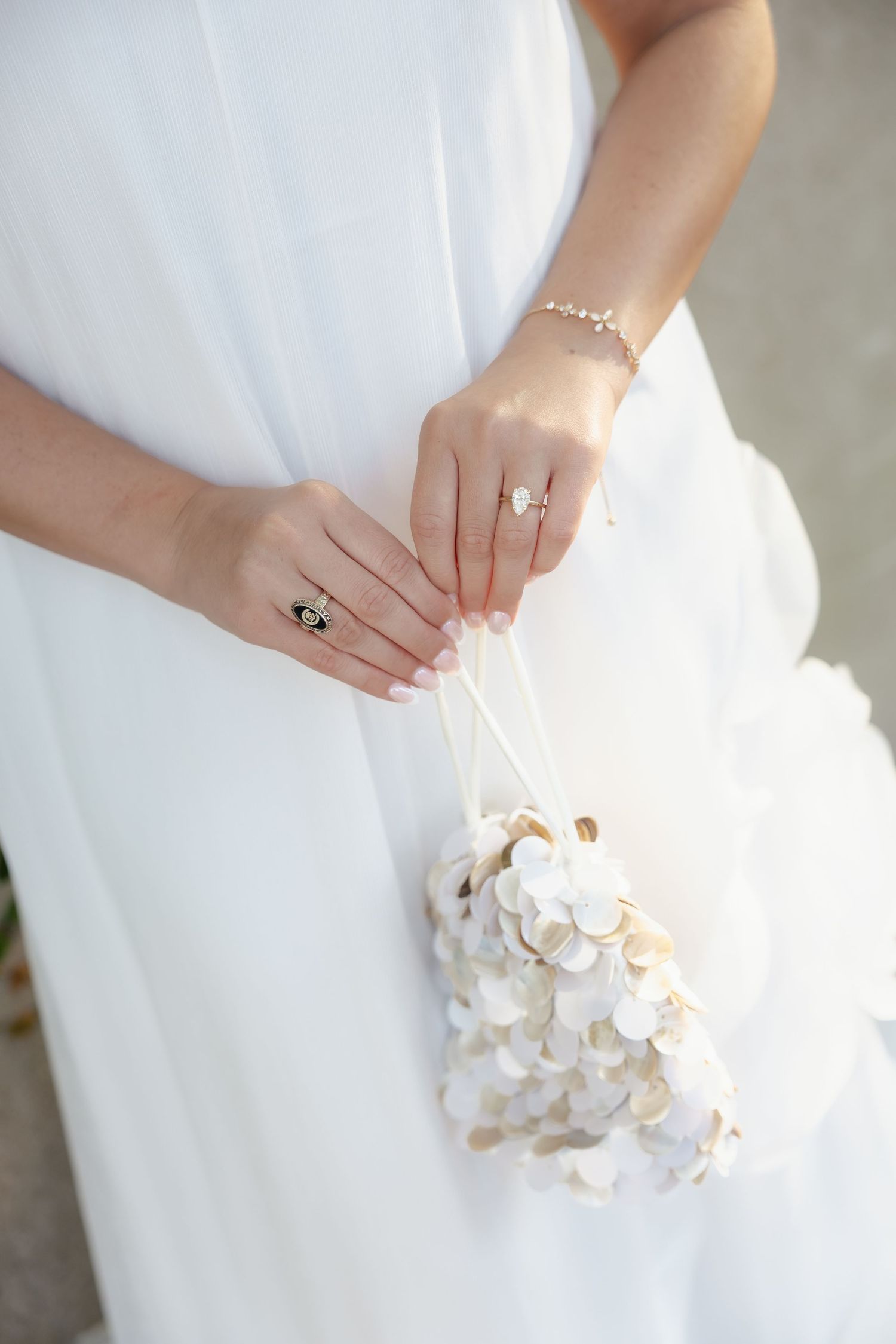 Bride in white dress holding delicate white floral bouquet with engagement ring and bracelet.