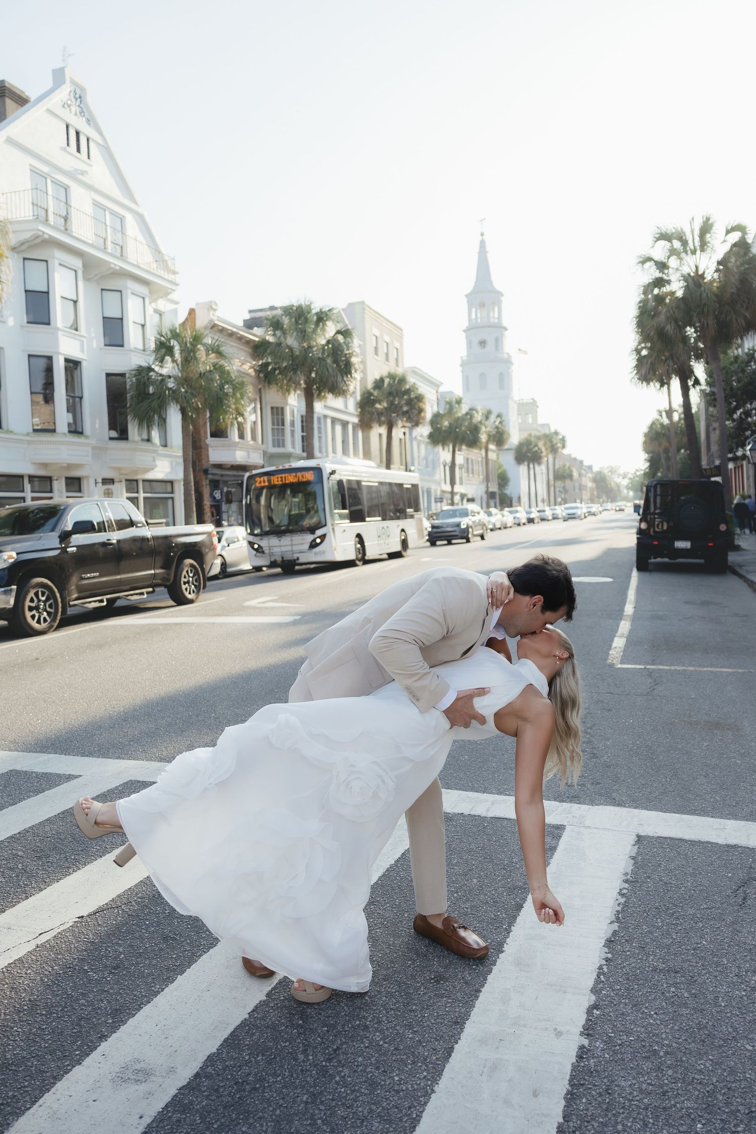 Groom dipping bride for a romantic kiss on a Charleston crosswalk with palm trees and steeple.