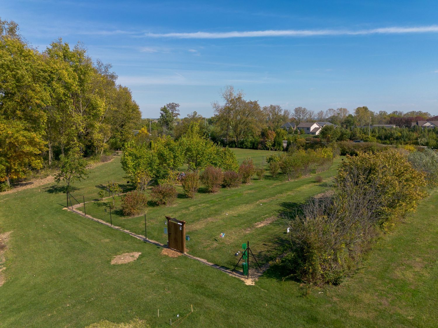 Aerial view of a sprawling golf course with rolling green hills and scattered trees under blue sky.
