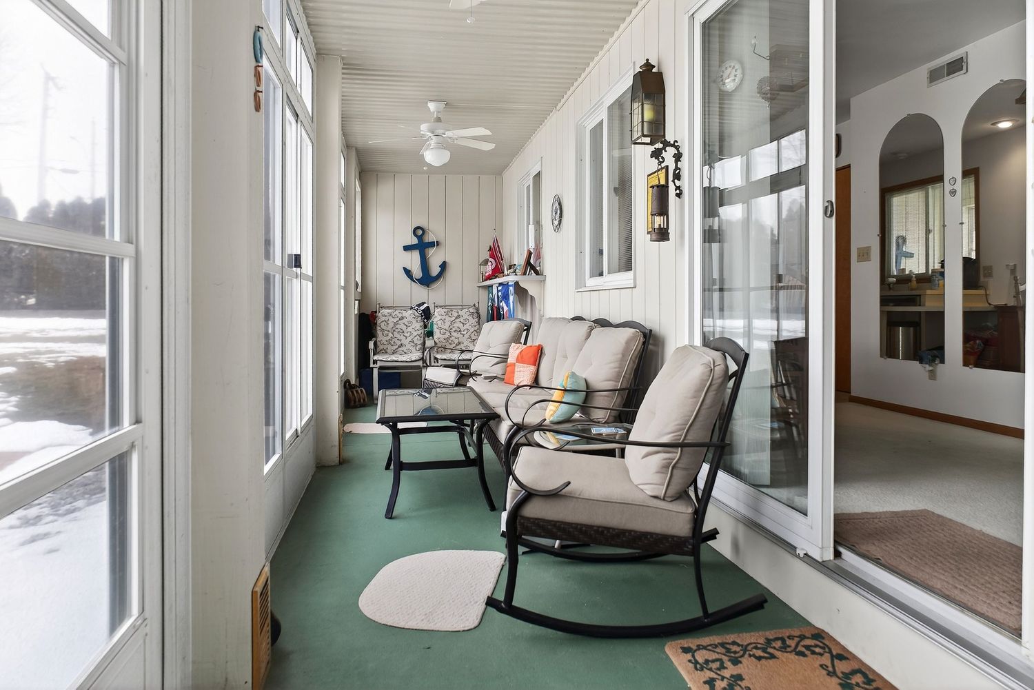 Sunlit coastal porch with multiple seating areas, white rocking chairs, and turquoise flooring overlooking the beach.