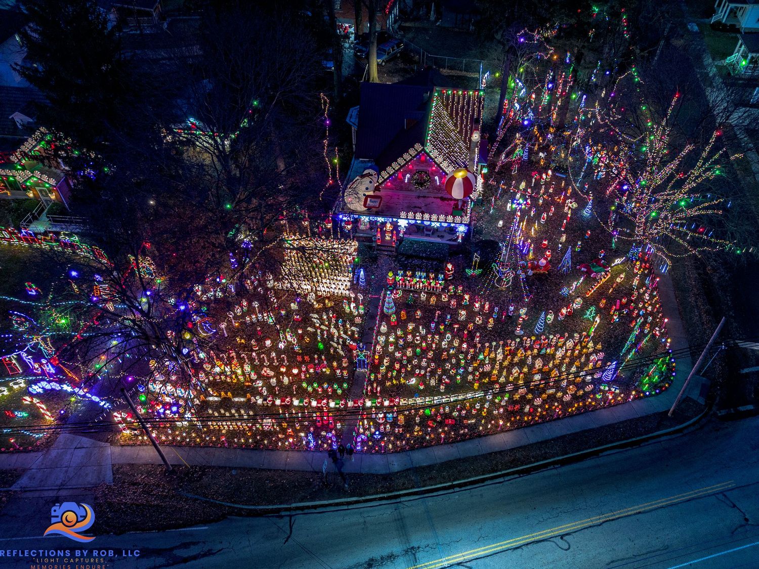 Nighttime aerial view of elaborate Christmas light display covering multiple houses and yards.