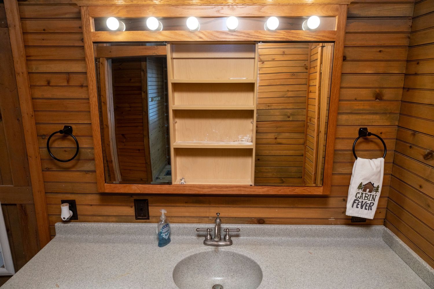 Bathroom vanity with mirror and lighting in log cabin style interior.