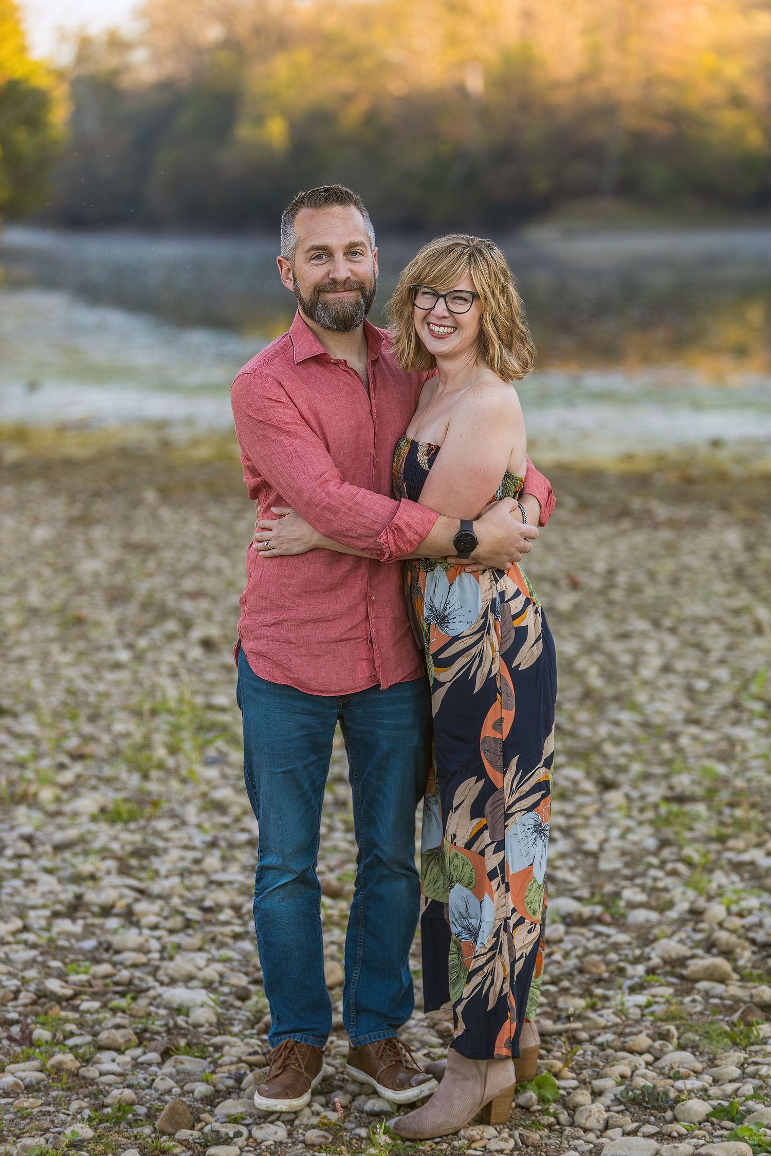 Couple embracing outdoors during golden hour autumn photoshoot with fallen leaves on ground.