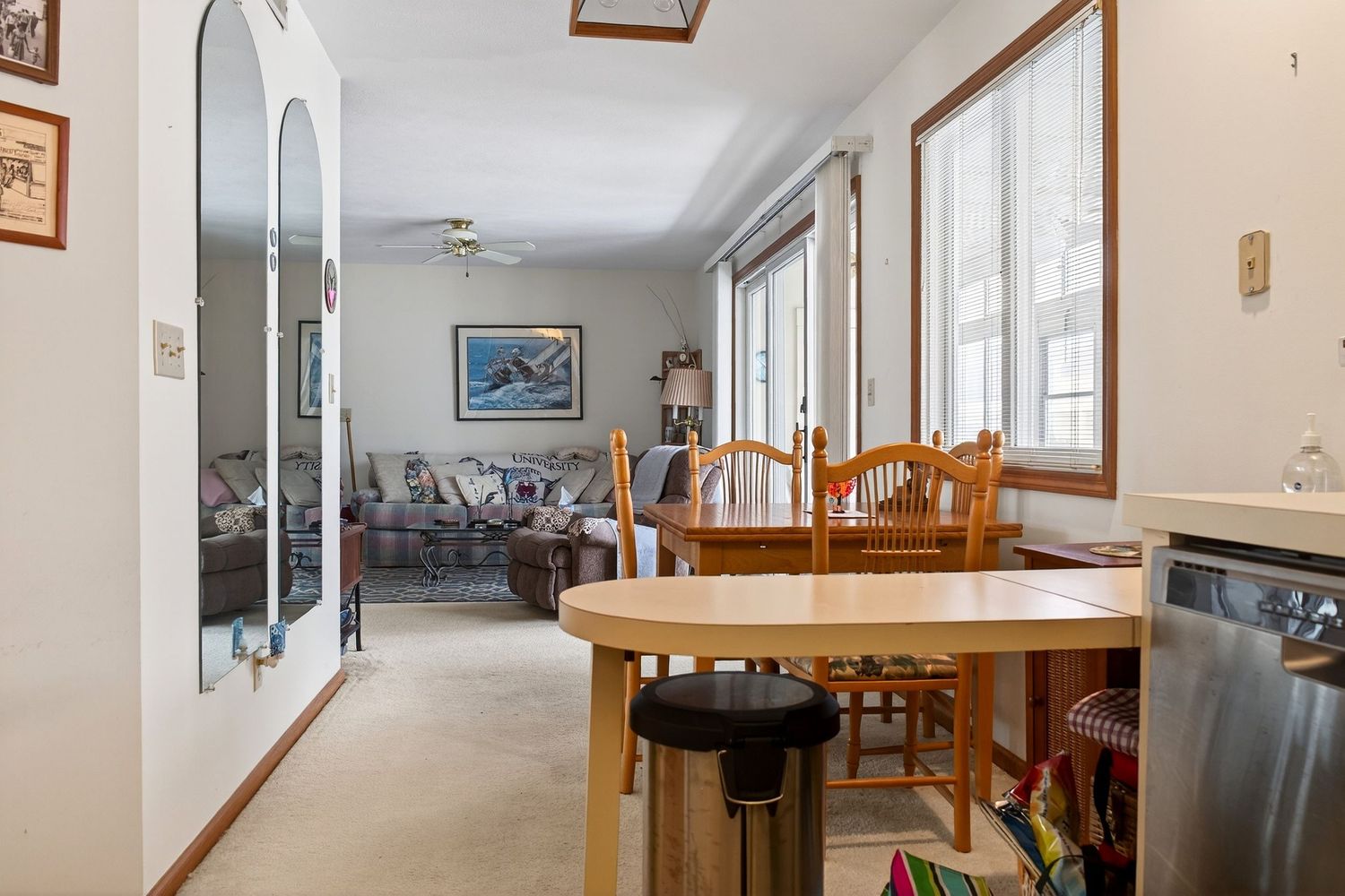 Bright sunroom with wooden dining table and chairs next to large windows overlooking living area with couch.
