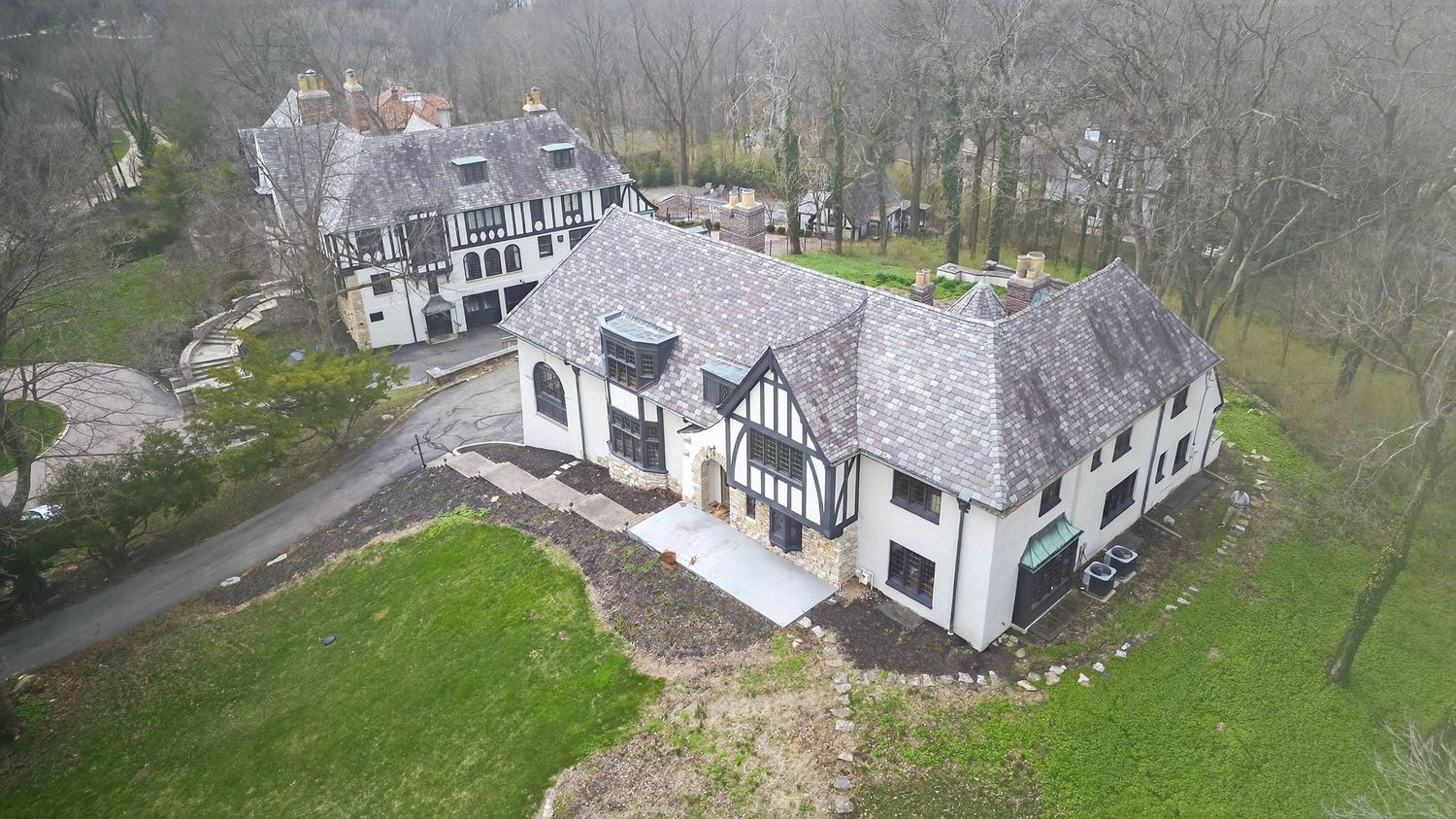 Aerial panoramic view of a historic stone cottage nestled in green countryside with surrounding stone walls and trees.