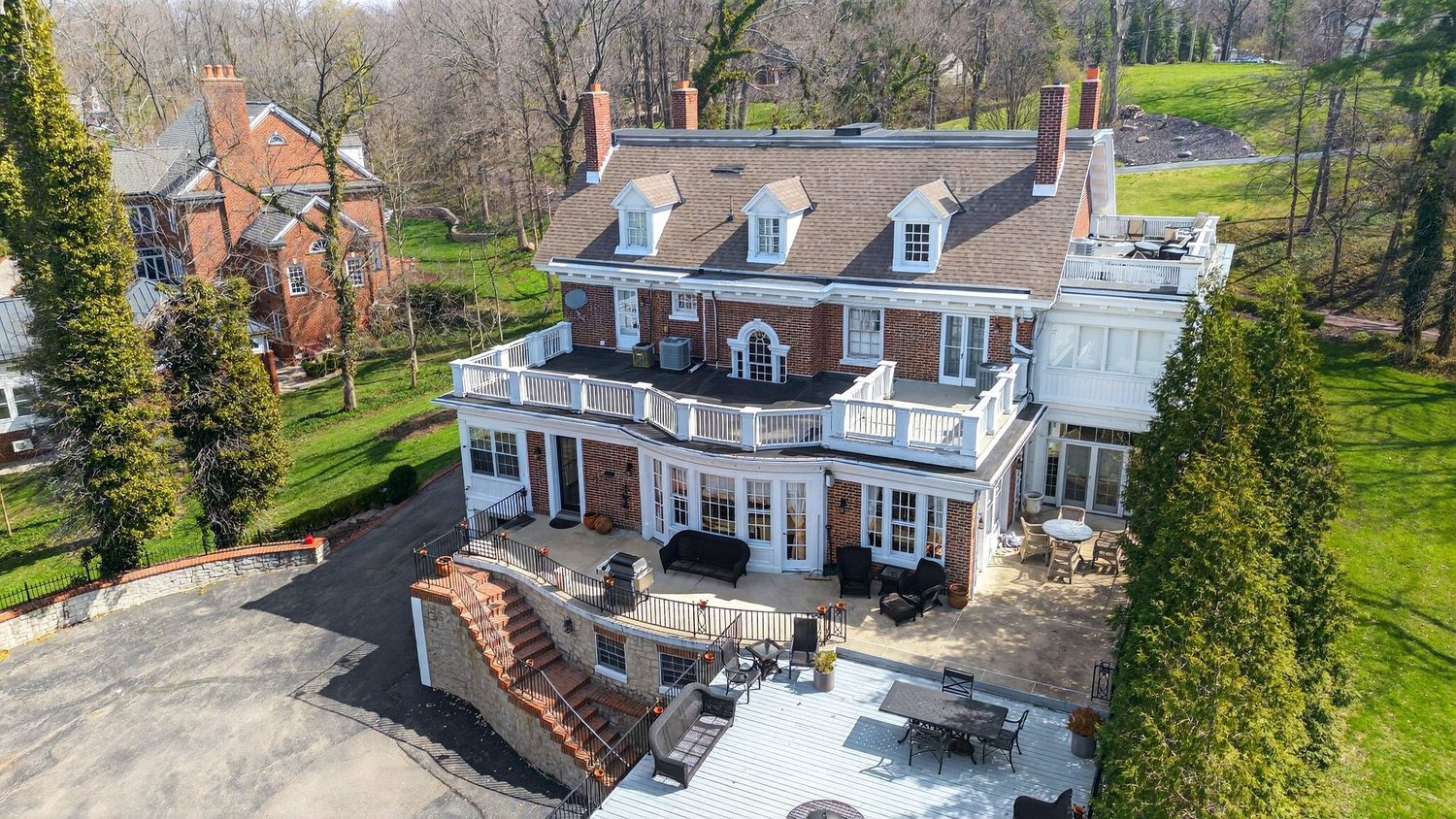 Aerial drone view of a classic colonial style home with dormers and brick exterior surrounded by winter trees.
