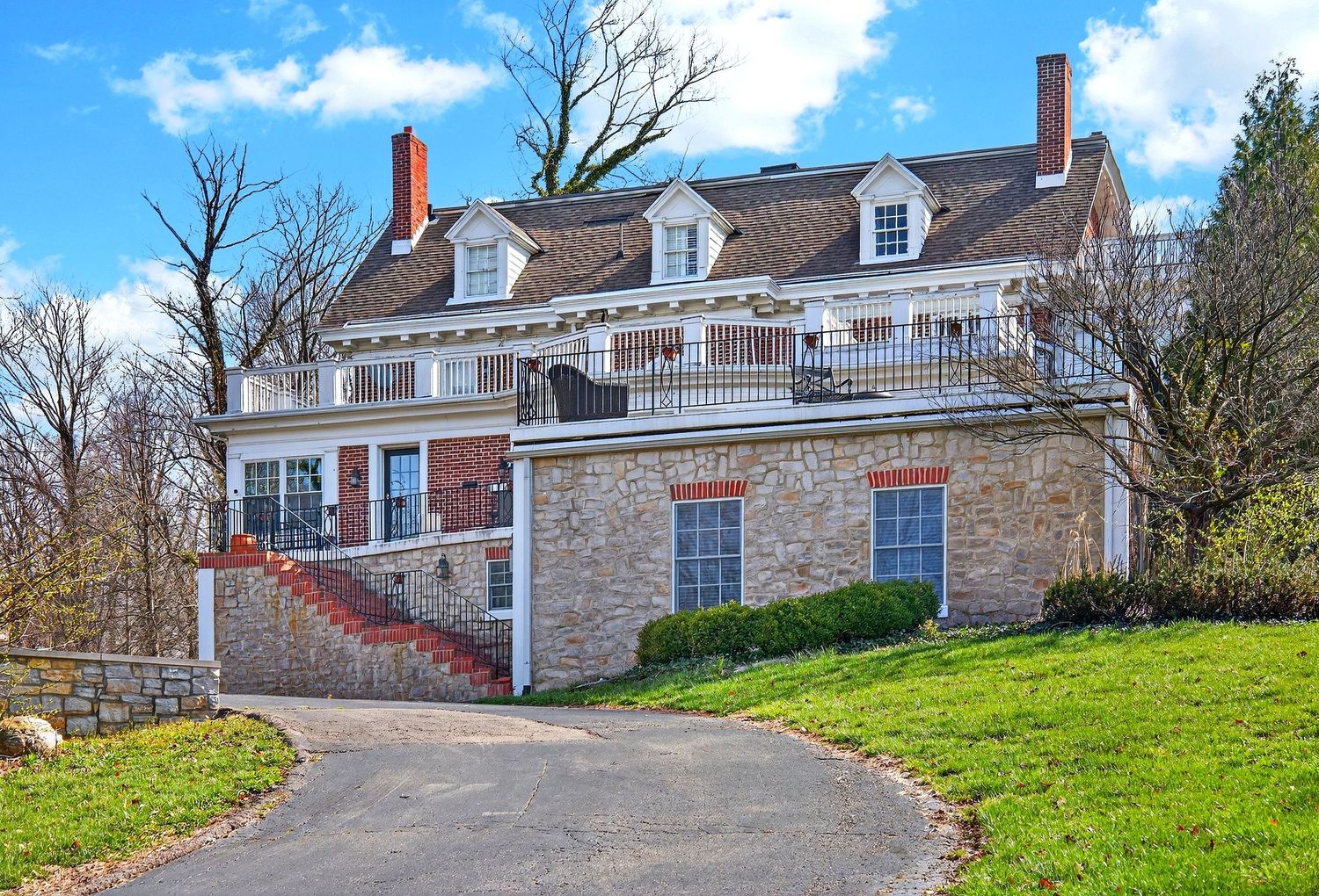 A panoramic view of historic stone buildings with dormers and white trim situated on a grassy hillside.