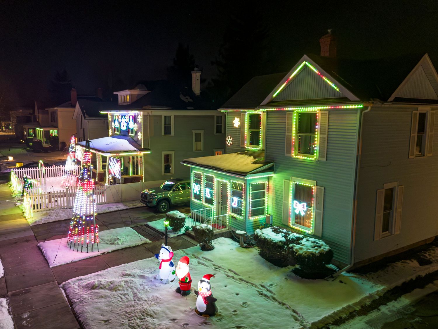 Row of houses lit up with festive Christmas lights and decorations in the snow.