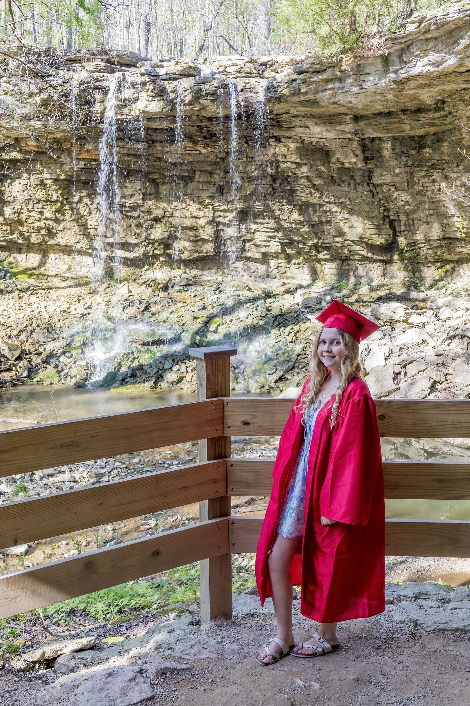 Red coat against limestone cliffs with wooden railing in a natural outdoor setting.