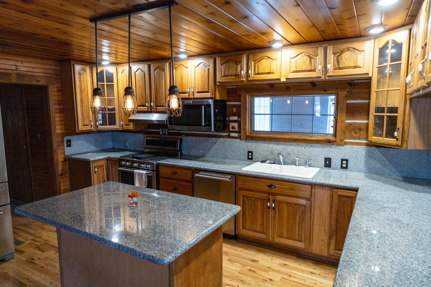 Modern kitchen with granite countertops and wooden cabinets in a log cabin setting.