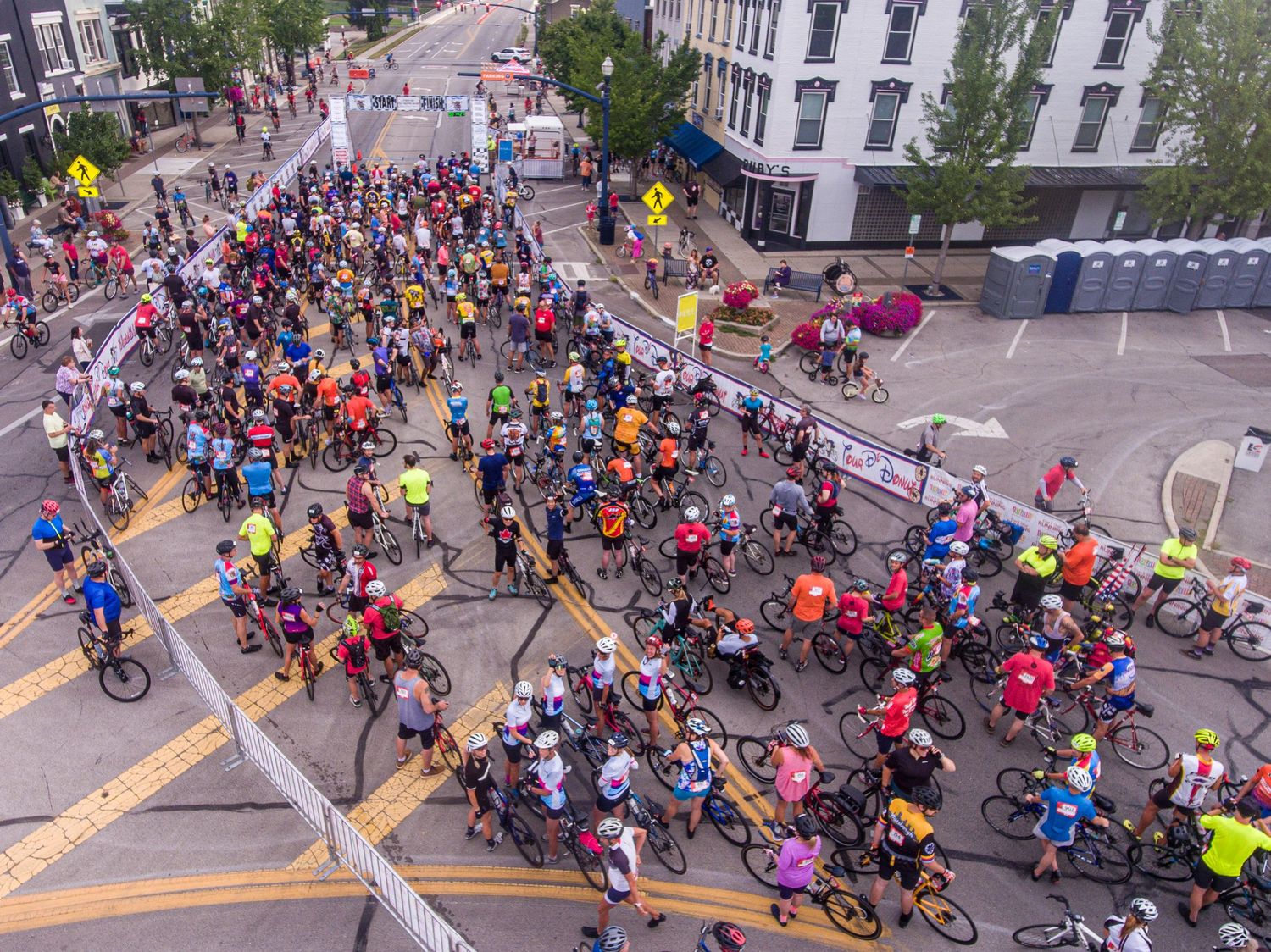 Aerial view of large crowd of cyclists gathering on city streets for an organized bike event.