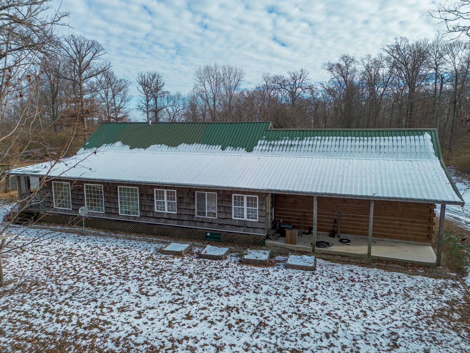 Long log cabin building with green metal roof and snow-dusted grounds in winter setting.