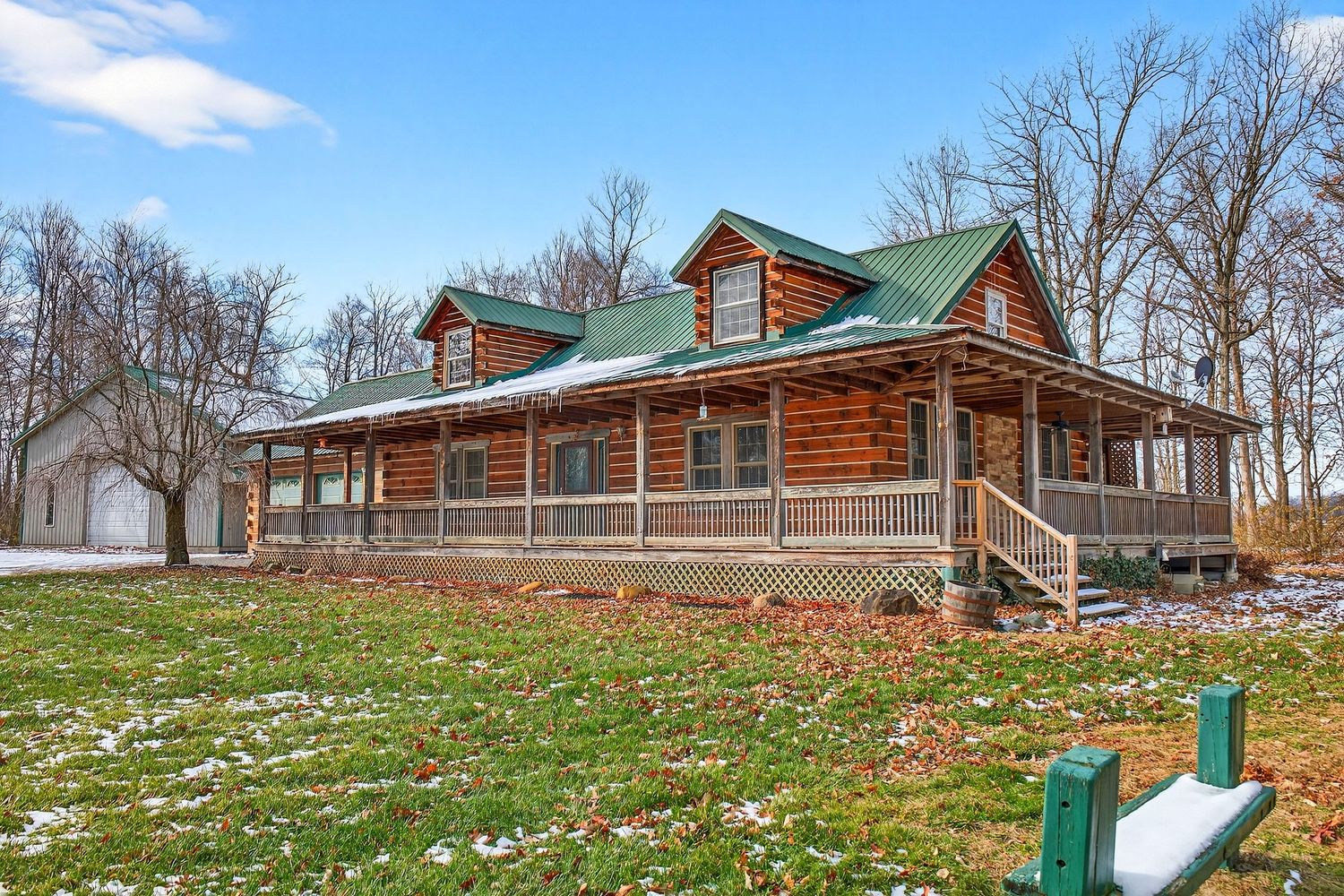 A panoramic view of a rustic log cabin retreat nestled among bare trees with a dusting of spring flowers on the ground.