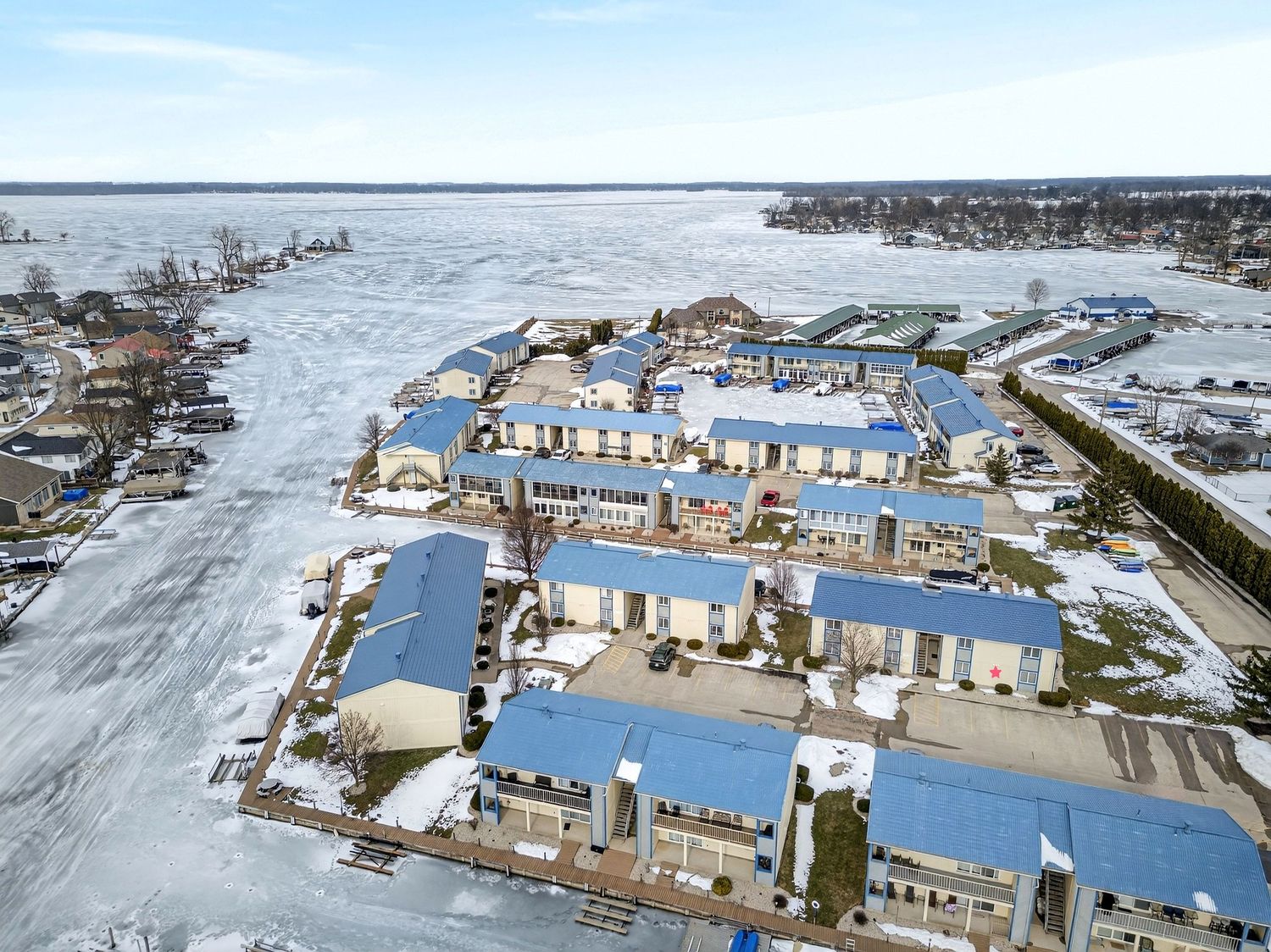 Aerial view of marina with boats and houses surrounded by frozen winter waters and snow-covered docks.