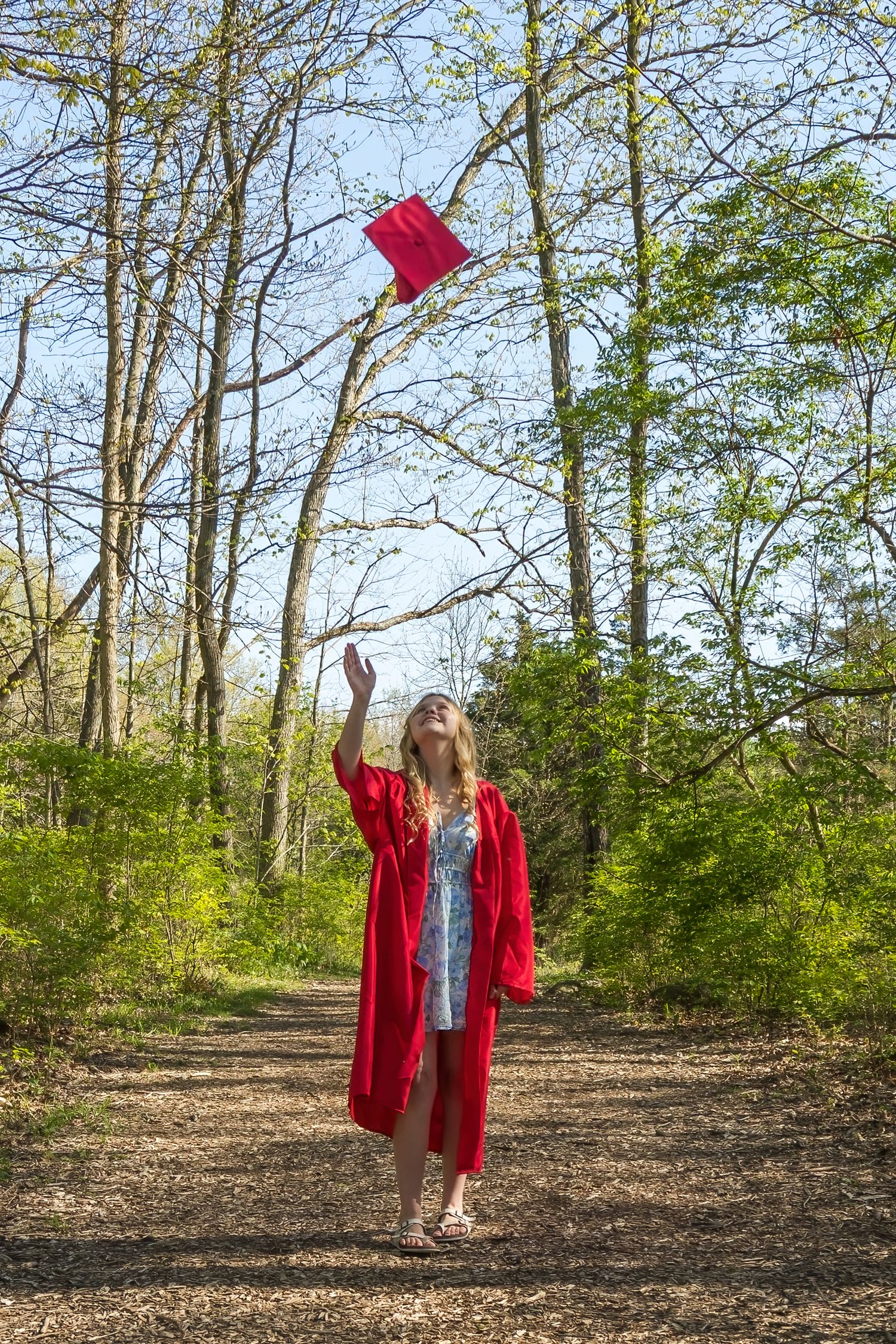 Person in a bright red coat walking through a wooded trail on a spring day.