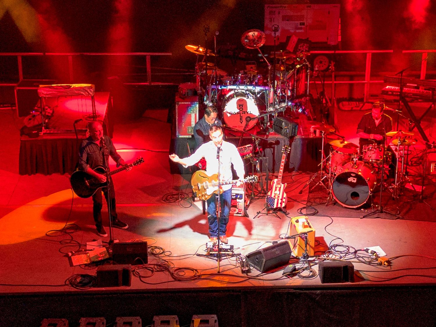 Concert stage illuminated in dramatic red lighting with performers and musical equipment.