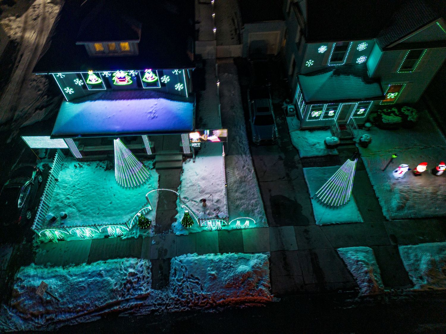 Houses decorated with blue and green holiday lights creating a magical winter wonderland scene at night.