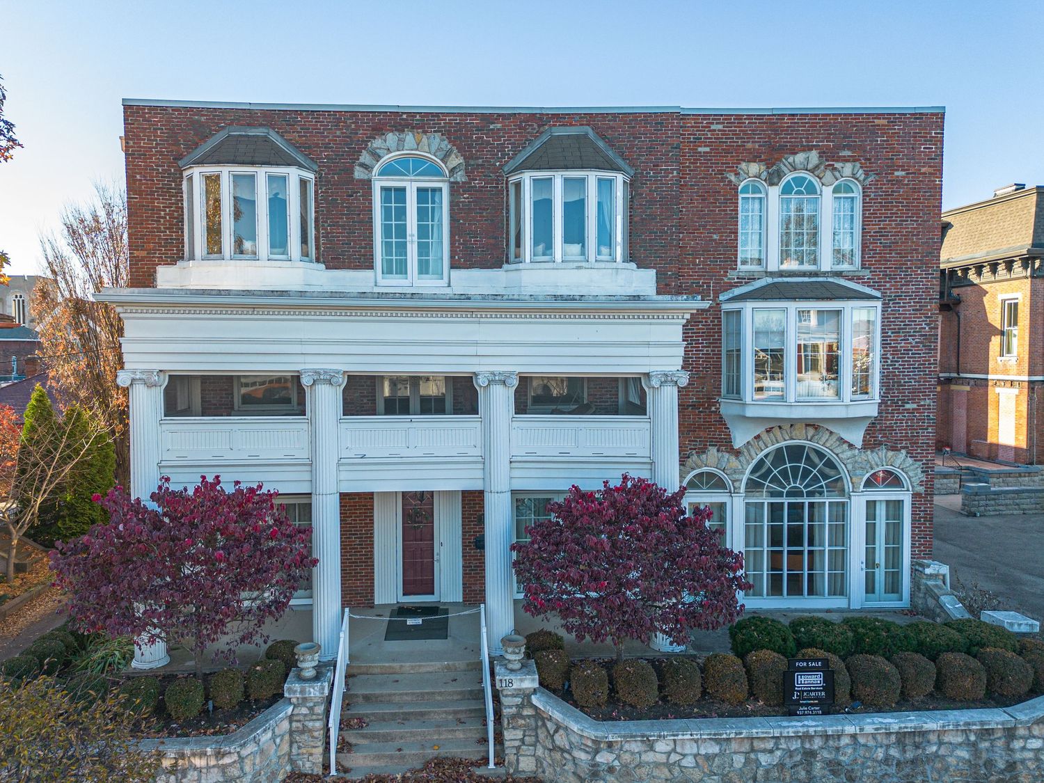 Elegant brick building with white columns and dormer windows featuring red maple trees in the landscaping.