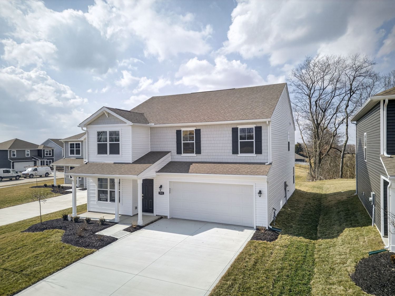 Modern white residential homes with attached garages sit along a gently sloping hillside in a new suburban development.