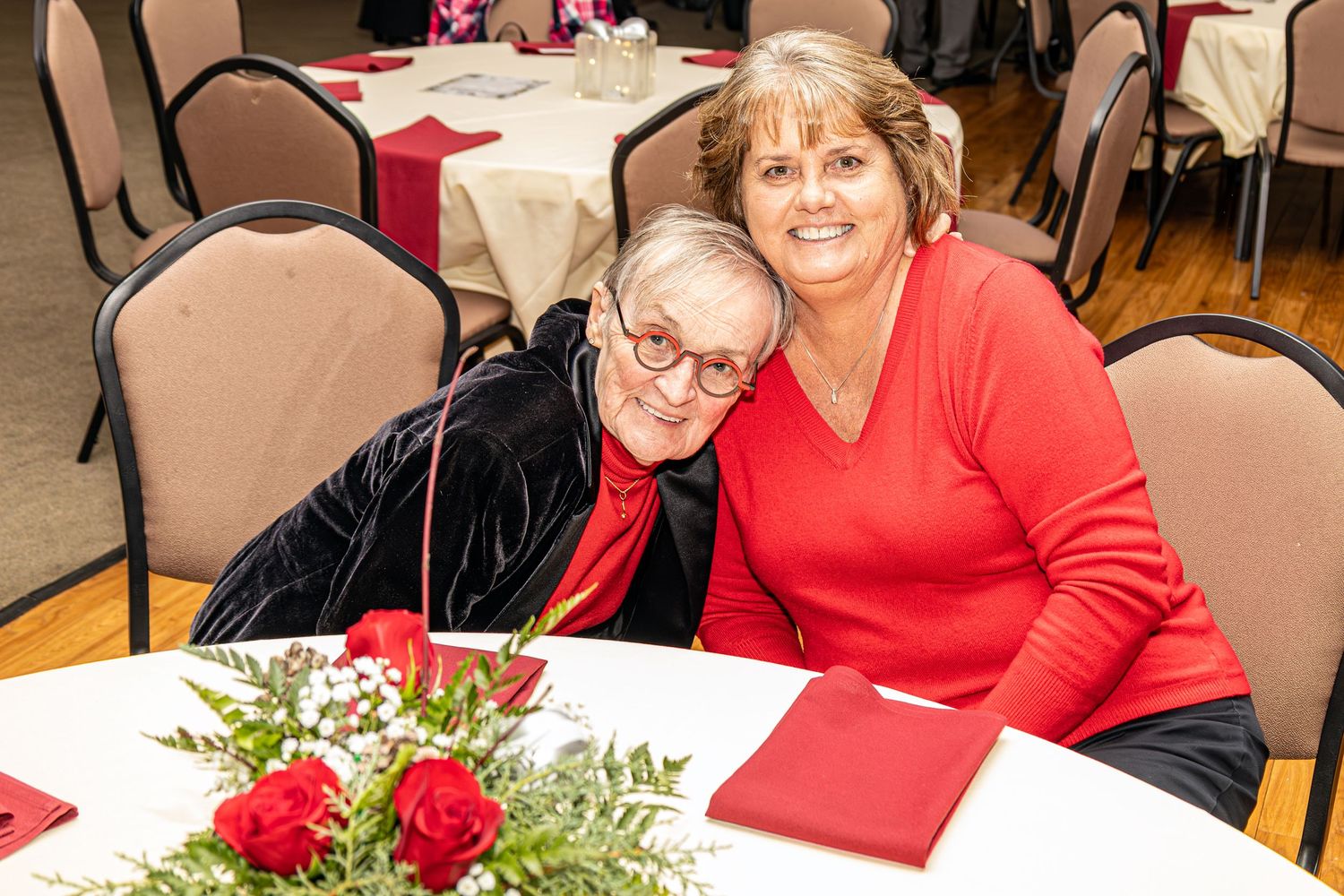 People seated at decorated tables with red tablecloths and floral centerpieces.