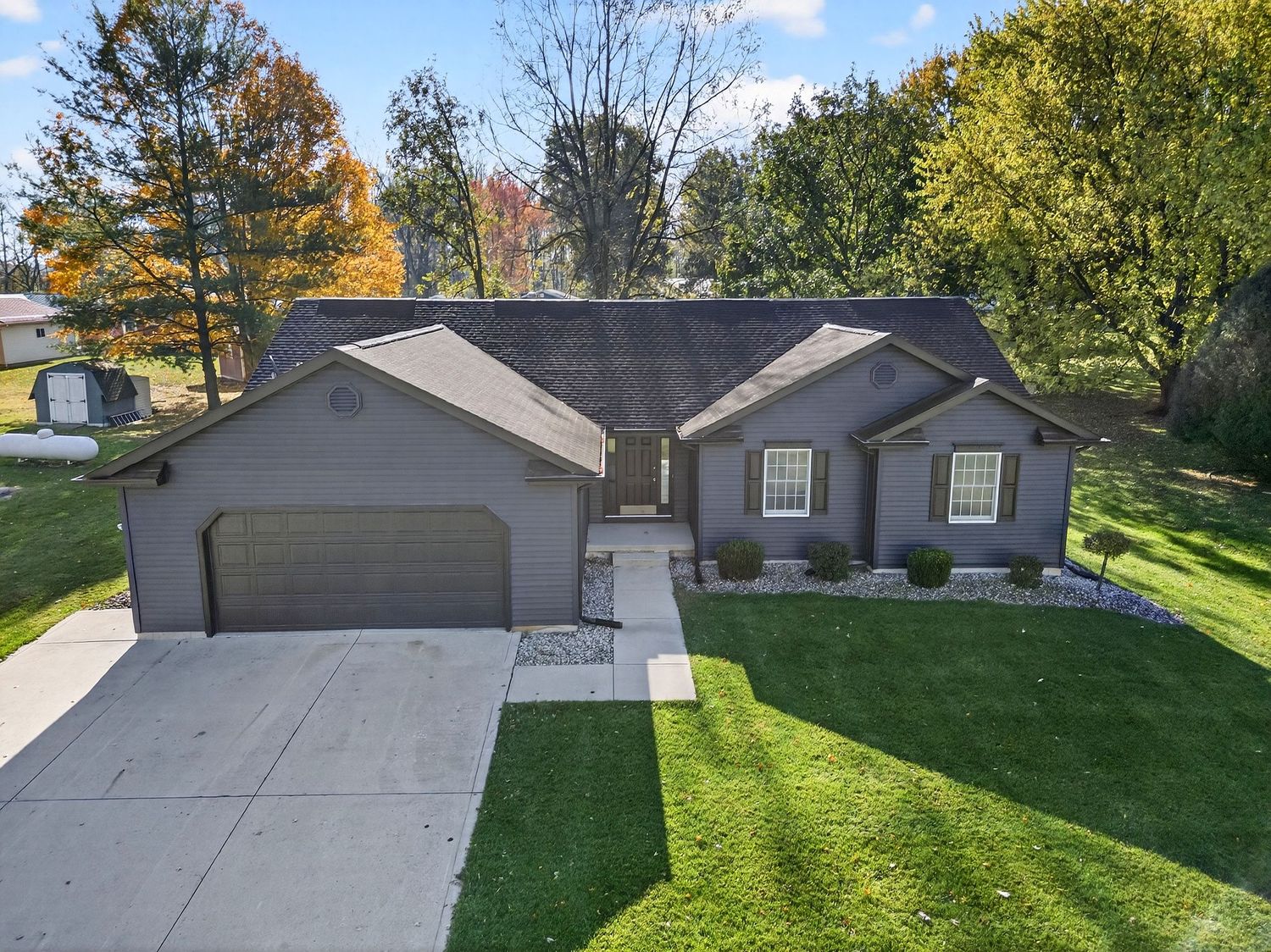 Aerial view of a residential home with a long driveway and well-maintained green lawn on a sunny autumn day.
