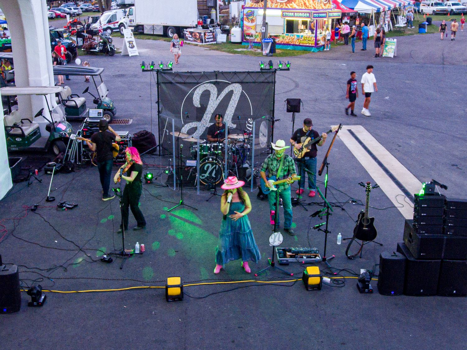 A band performs on an outdoor stage with green lighting and musical equipment setup.