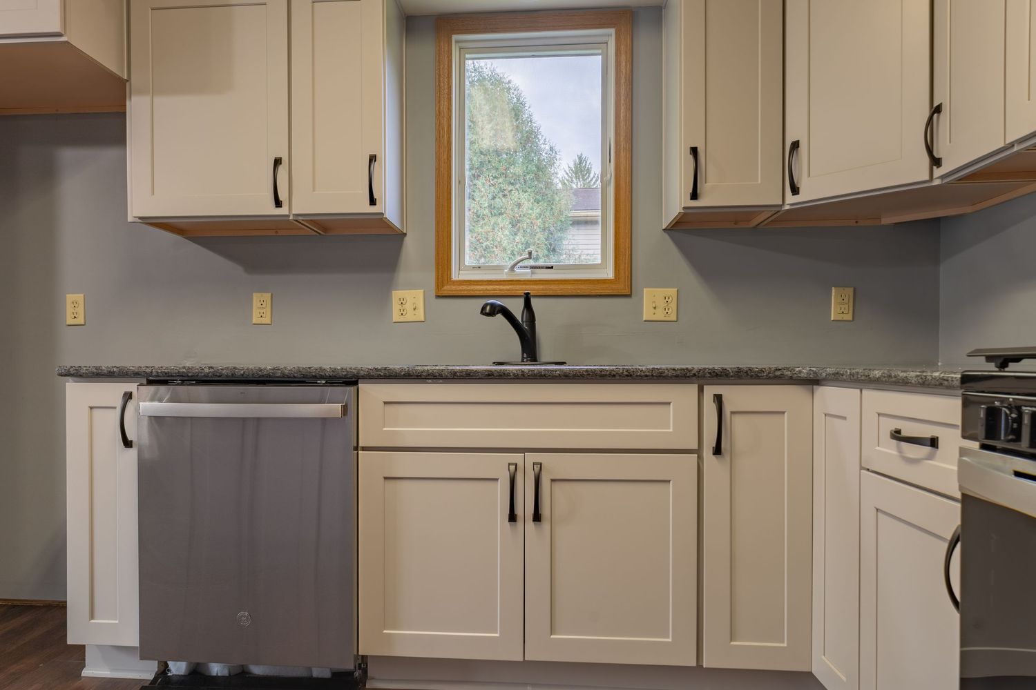 Modern kitchen with light gray cabinets, stainless appliances, and dark countertops.