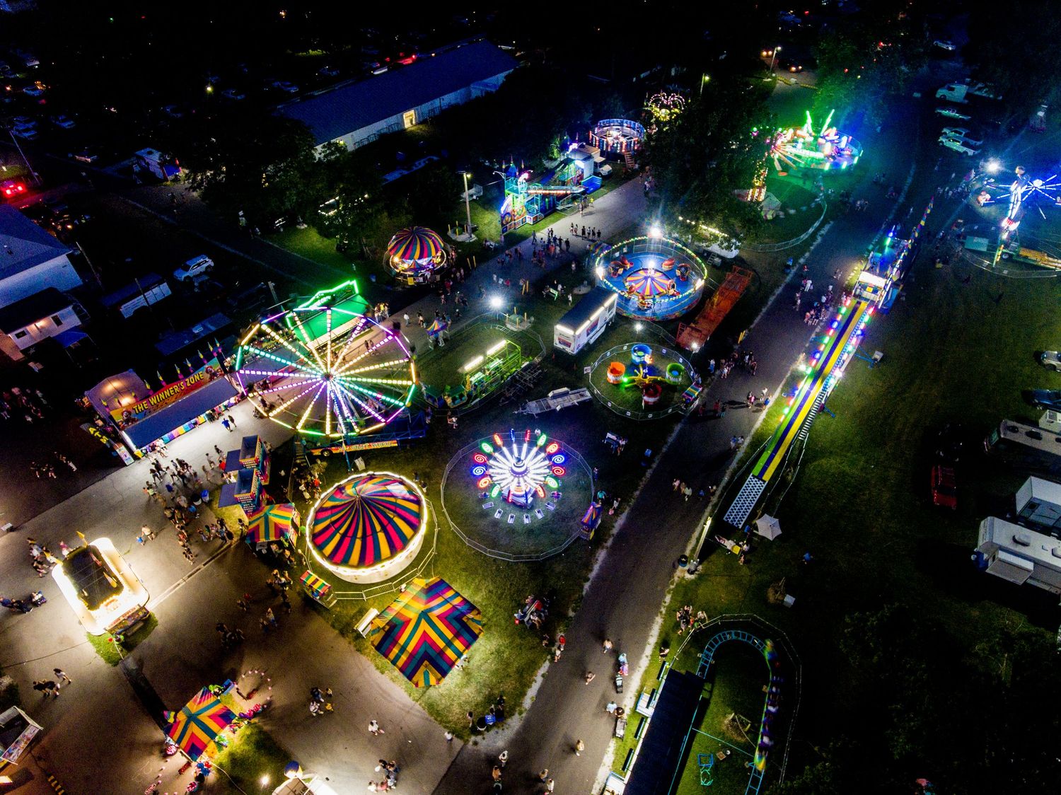 Aerial view of carnival at night with colorful illuminated rides and attractions.