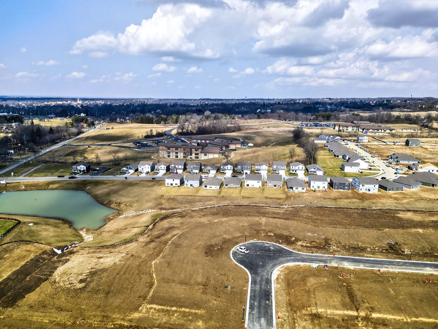 Aerial view of a new residential development with homes and infrastructure being built around a small pond.