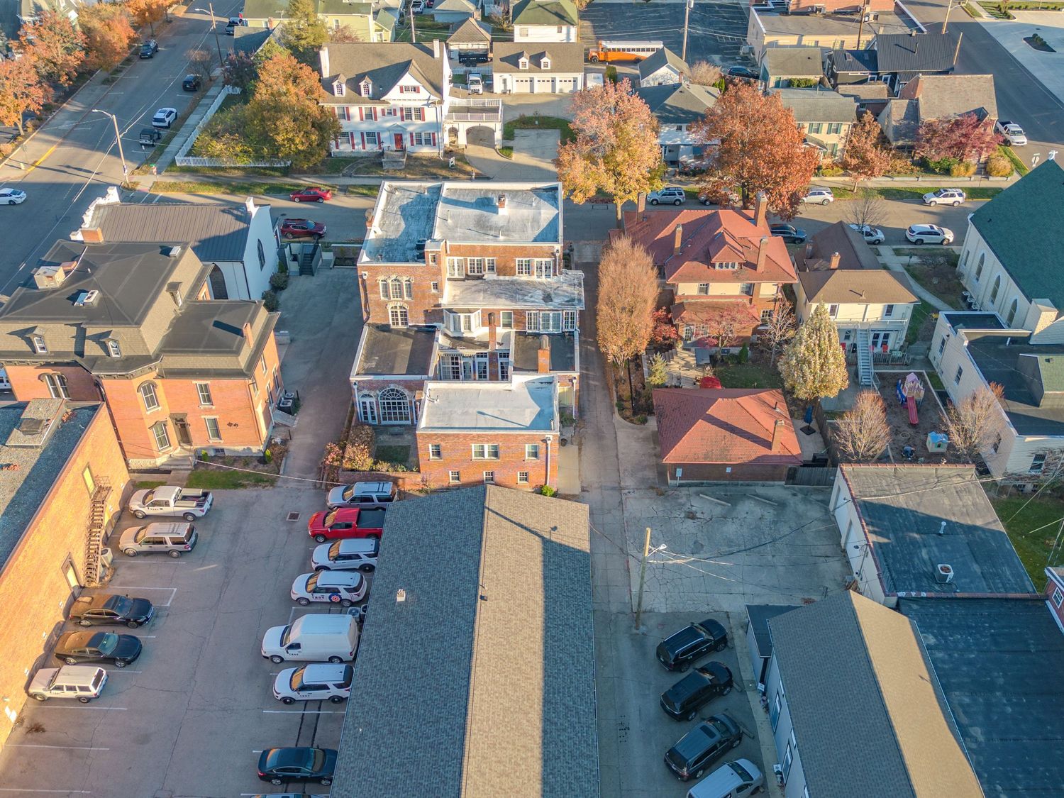 Aerial view of a small town neighborhood with autumn trees and parked cars along commercial buildings.