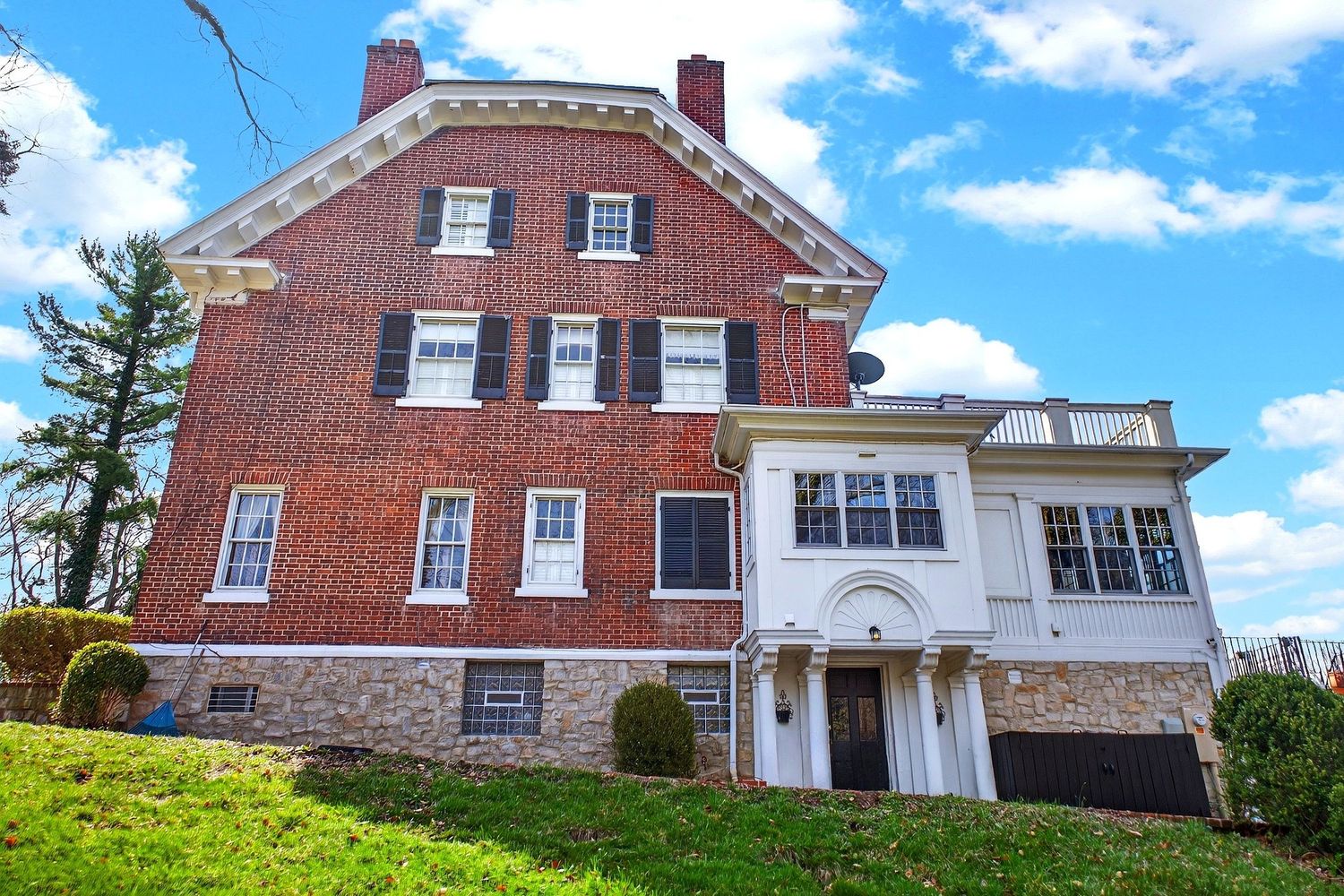 A panoramic view of a historic red brick mansion with white trim and multiple chimneys against a bright blue sky.