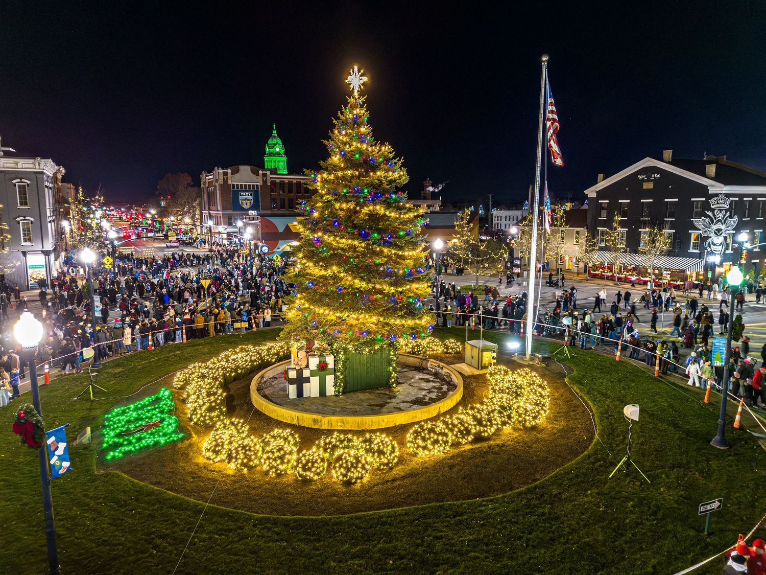 Panoramic view of a town square illuminated with golden Christmas lights and decorations at night.