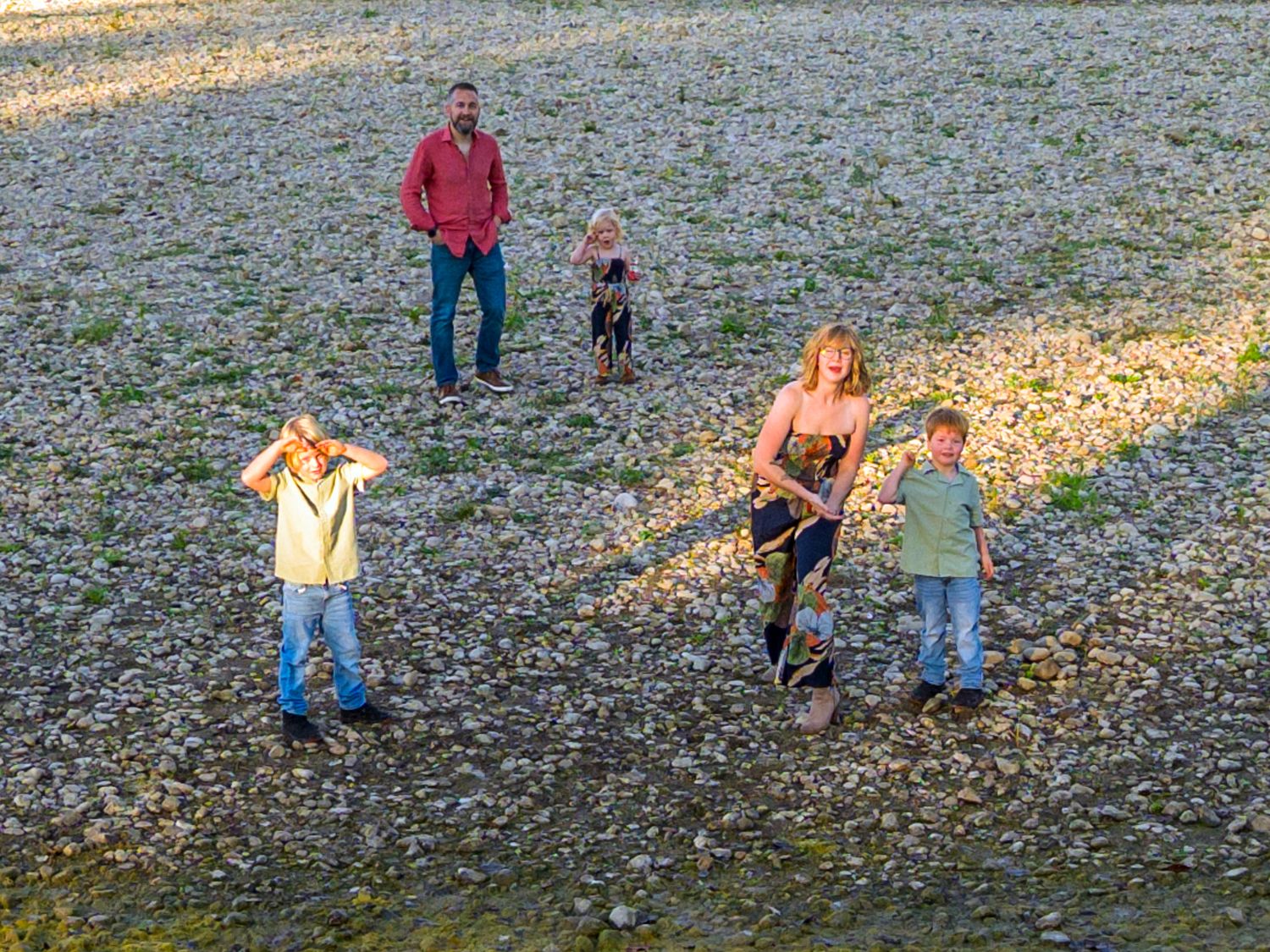 Family group playing and walking on rocky ground during golden hour.