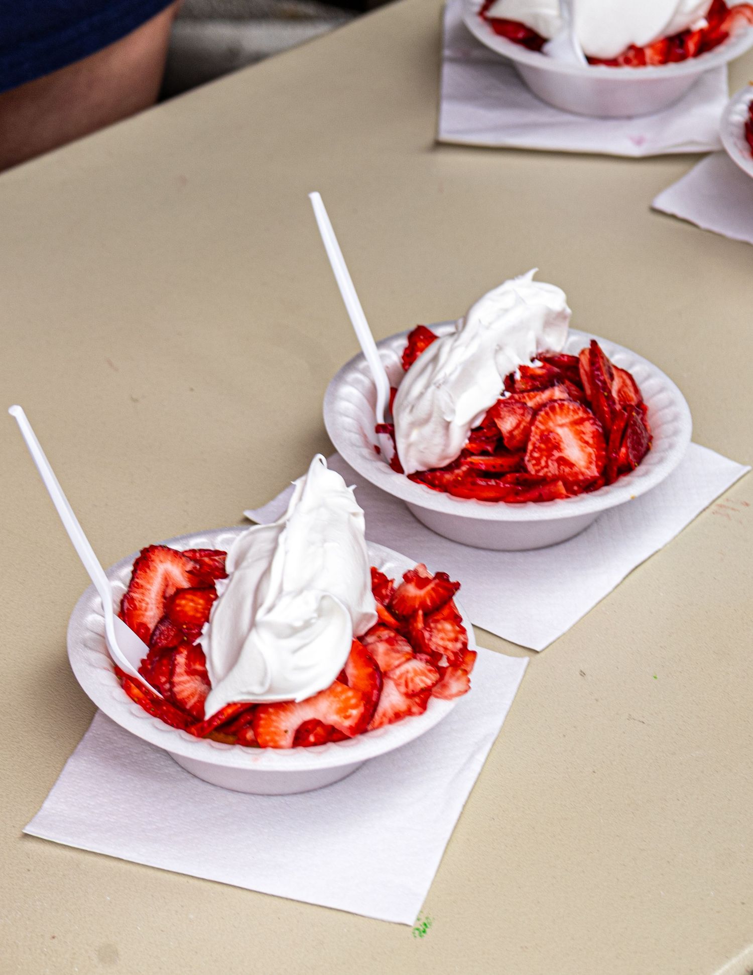Fresh strawberry desserts with whipped cream served on white paper plates.