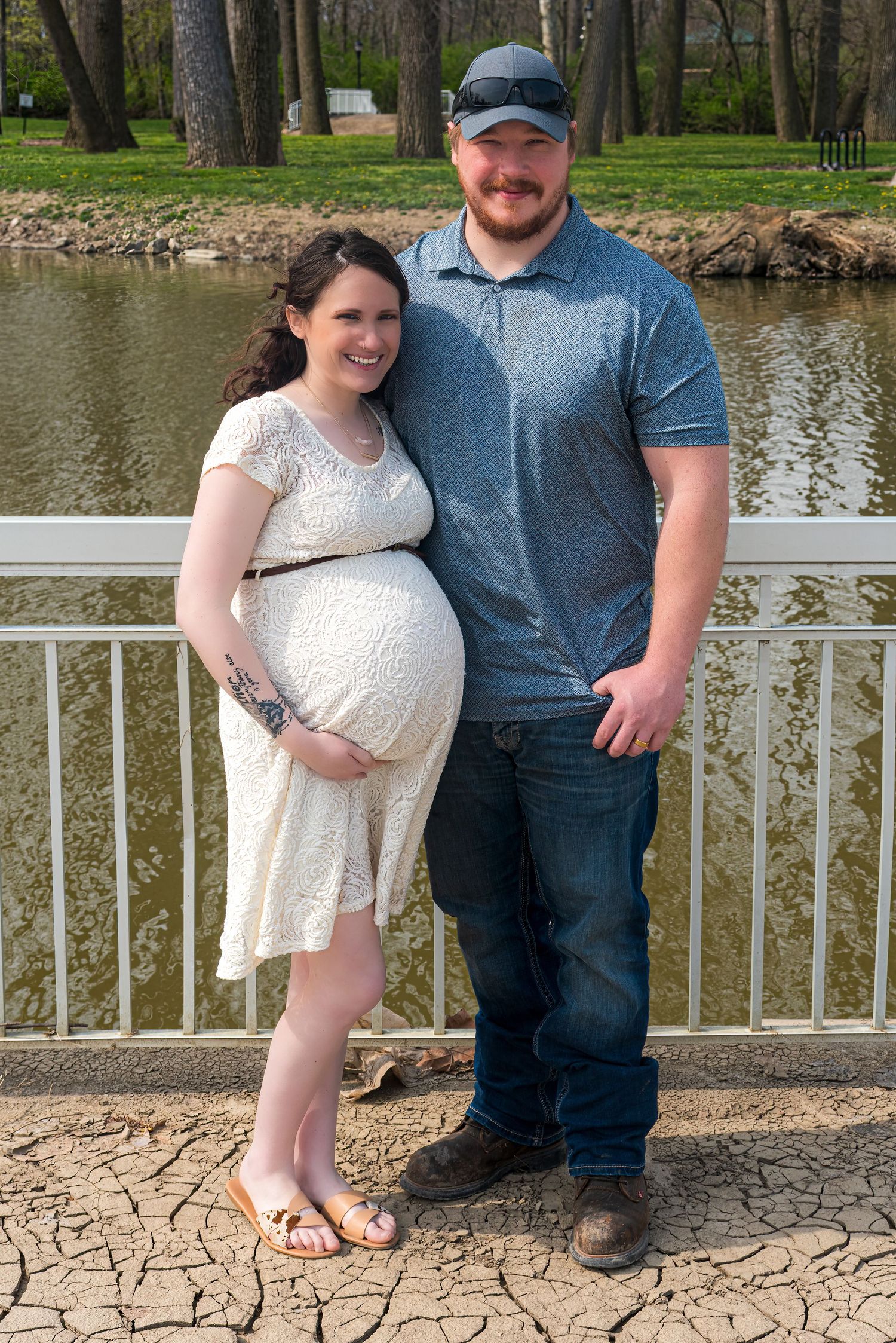 Couple poses together on a stone patio overlooking a pond with trees in the background.