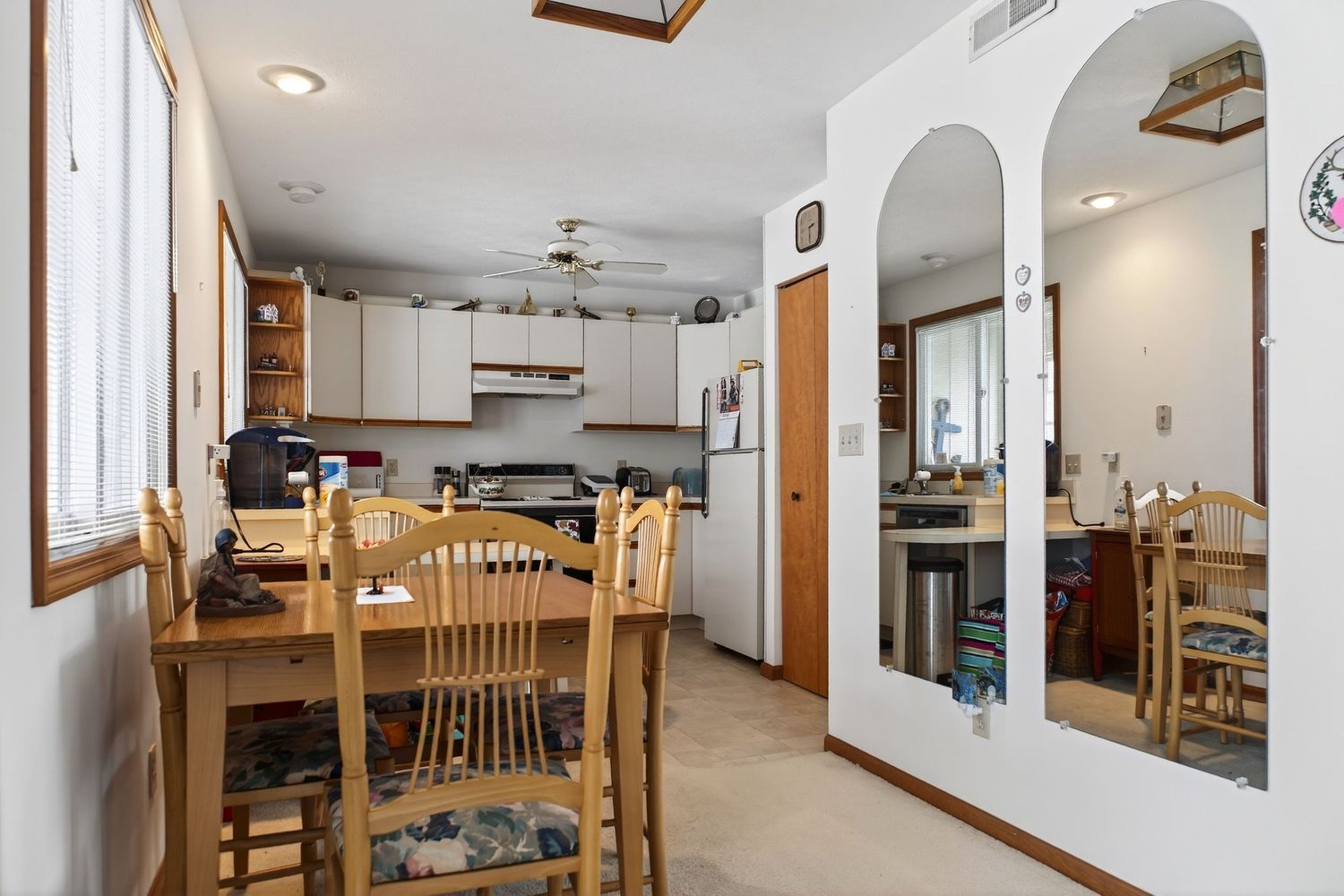 Bright kitchen and dining area with wooden table, chairs, white cabinets and arched wall opening.