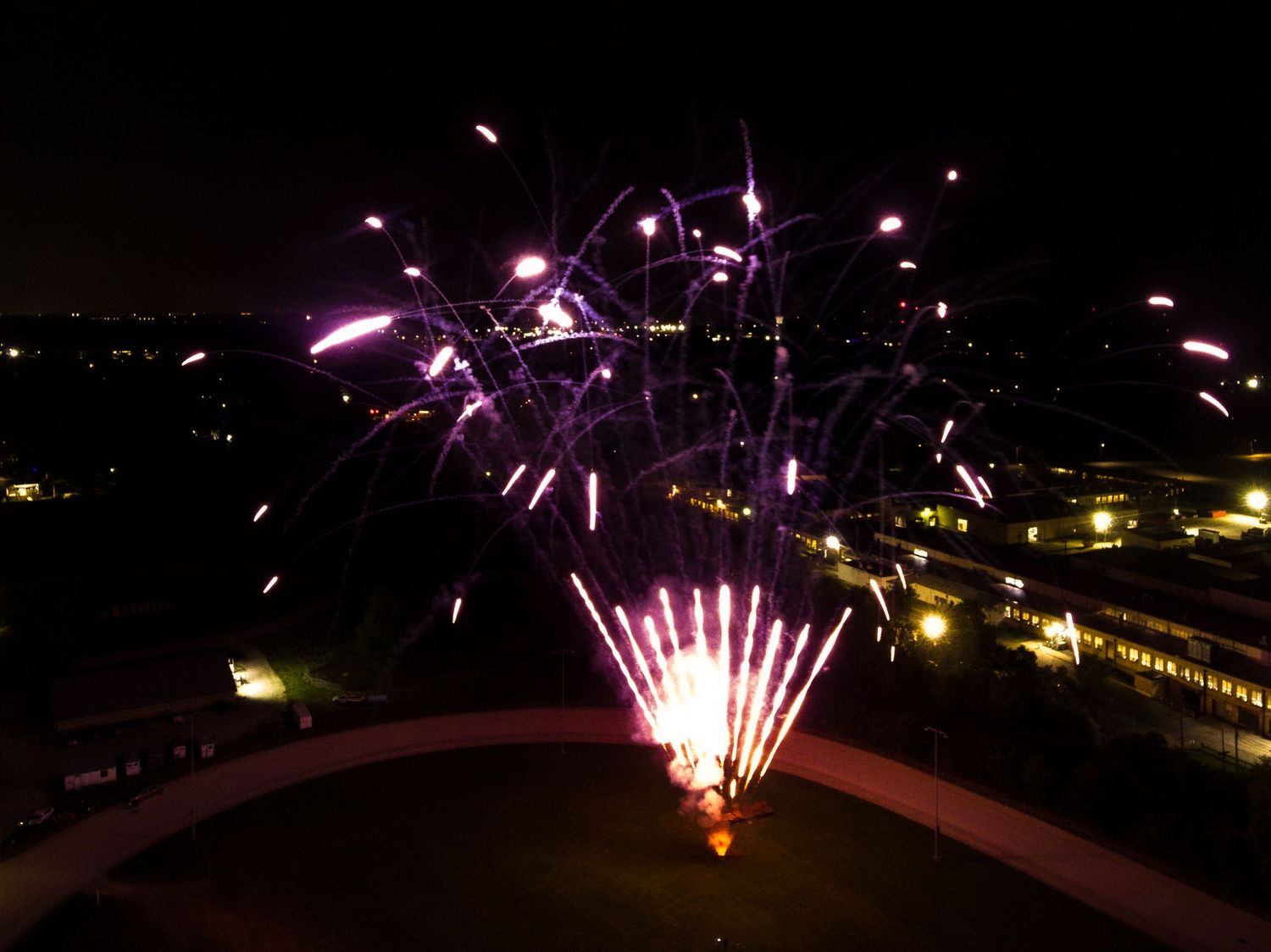 Colorful pink fireworks display lighting up night sky over venue.