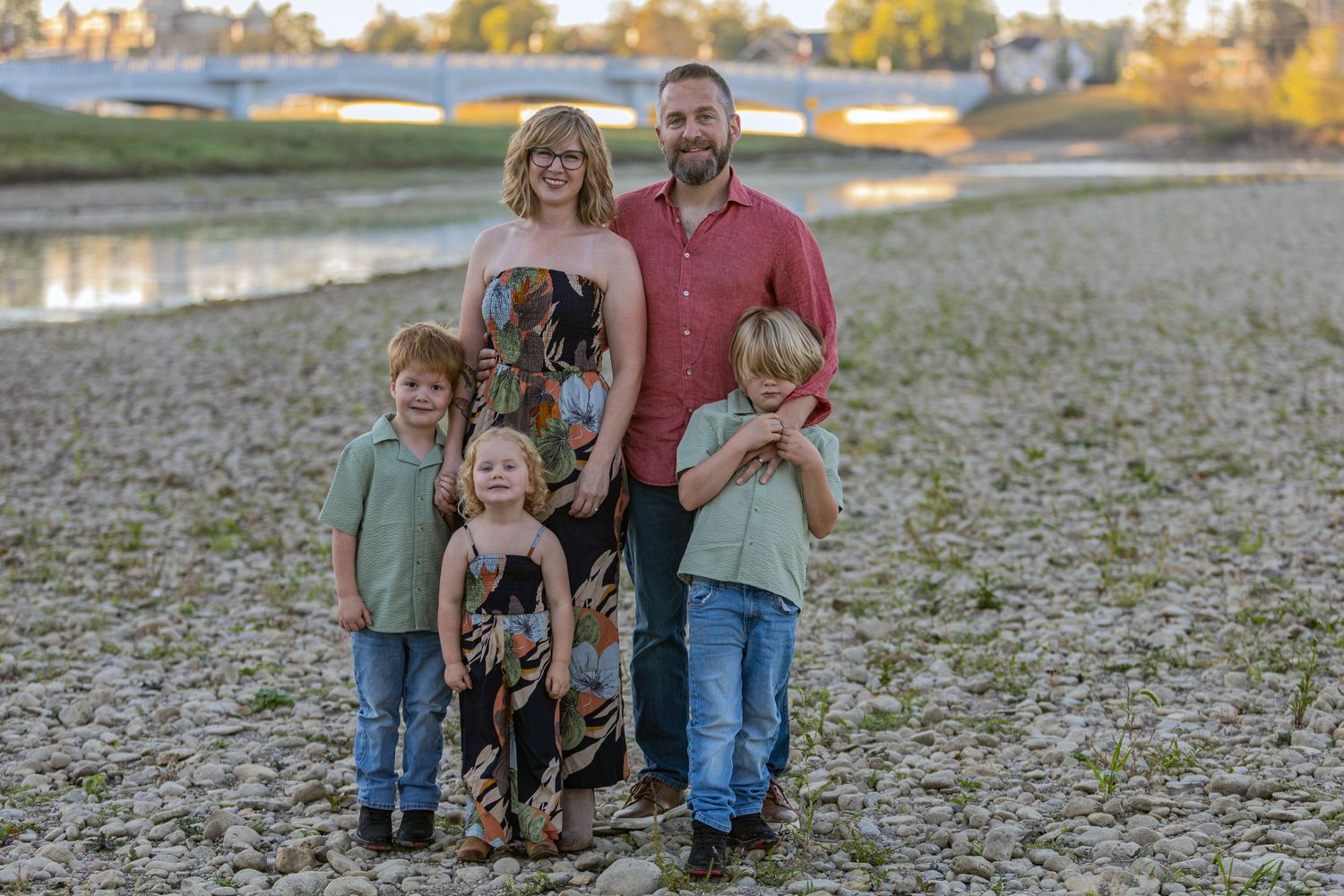 A family poses together outdoors during golden hour in a natural setting.