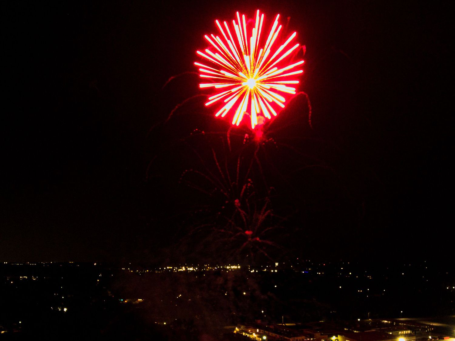 Bright red firework explosion illuminating the night sky over a cityscape.