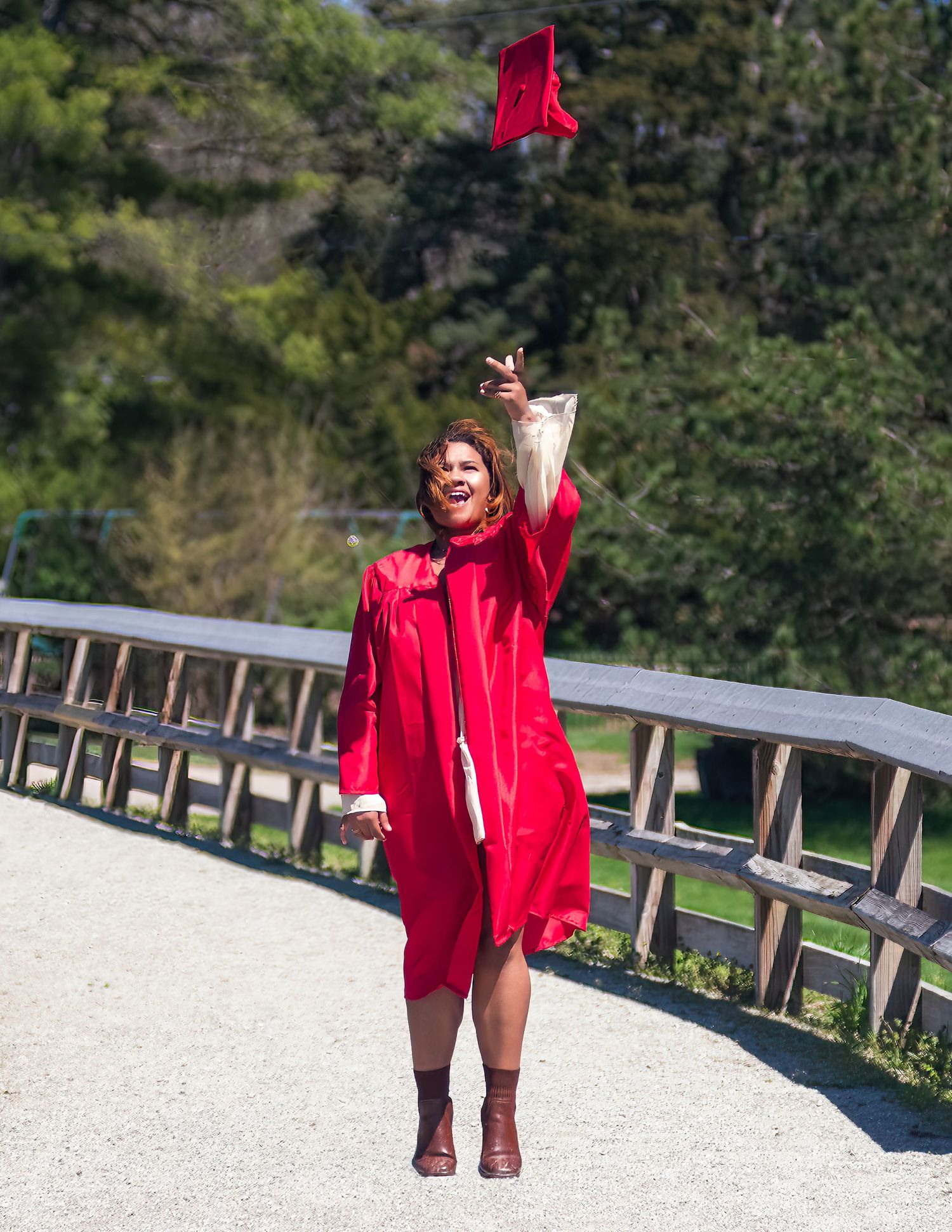 A graduate in red academic regalia celebrates on a pathway outdoors.