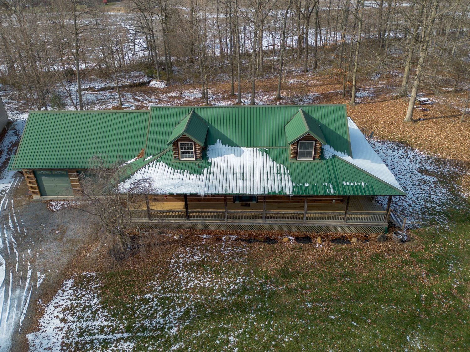 Rustic wooden lodge buildings with green roofs nestled among trees in light winter snow.