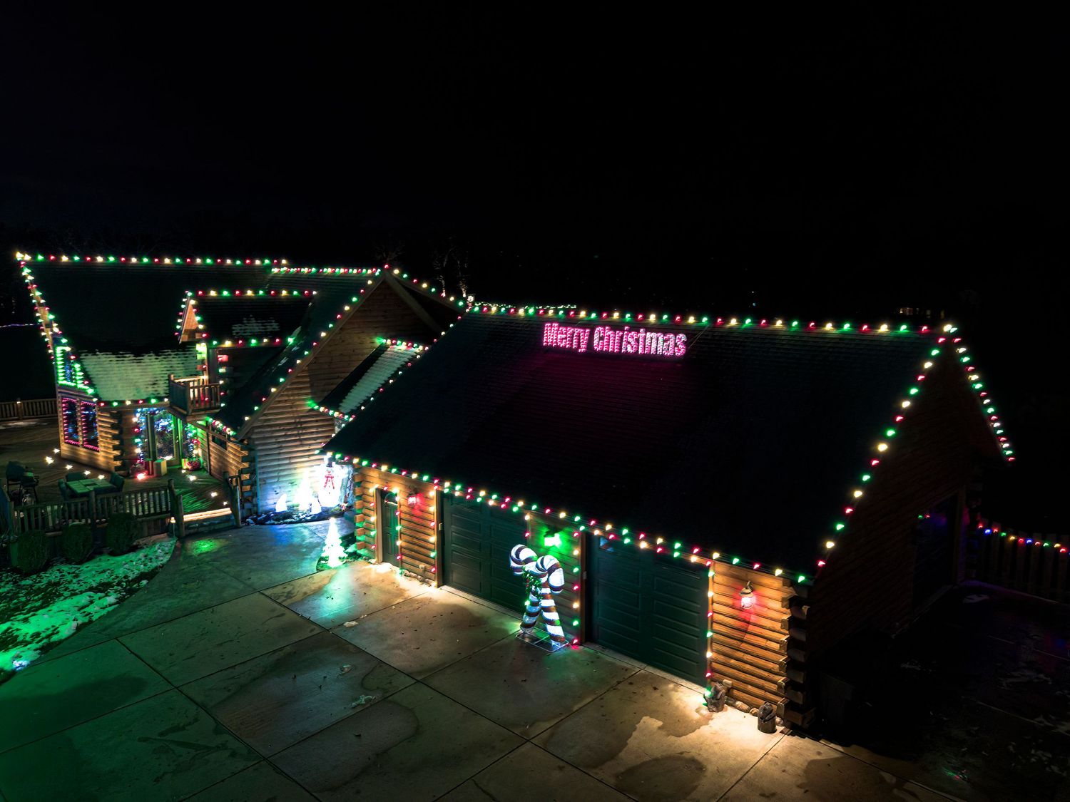Colorful Christmas lights illuminate a snowy winter scene with decorated buildings and trees.