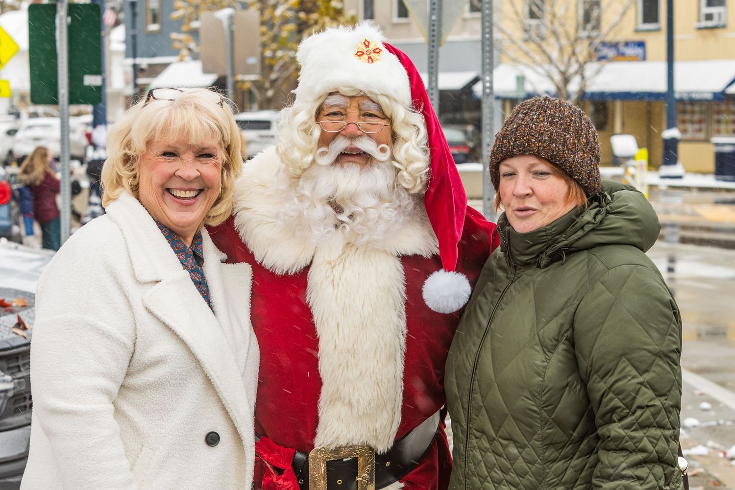 Santa Claus greets visitors during a snowy winter celebration in a small town setting.