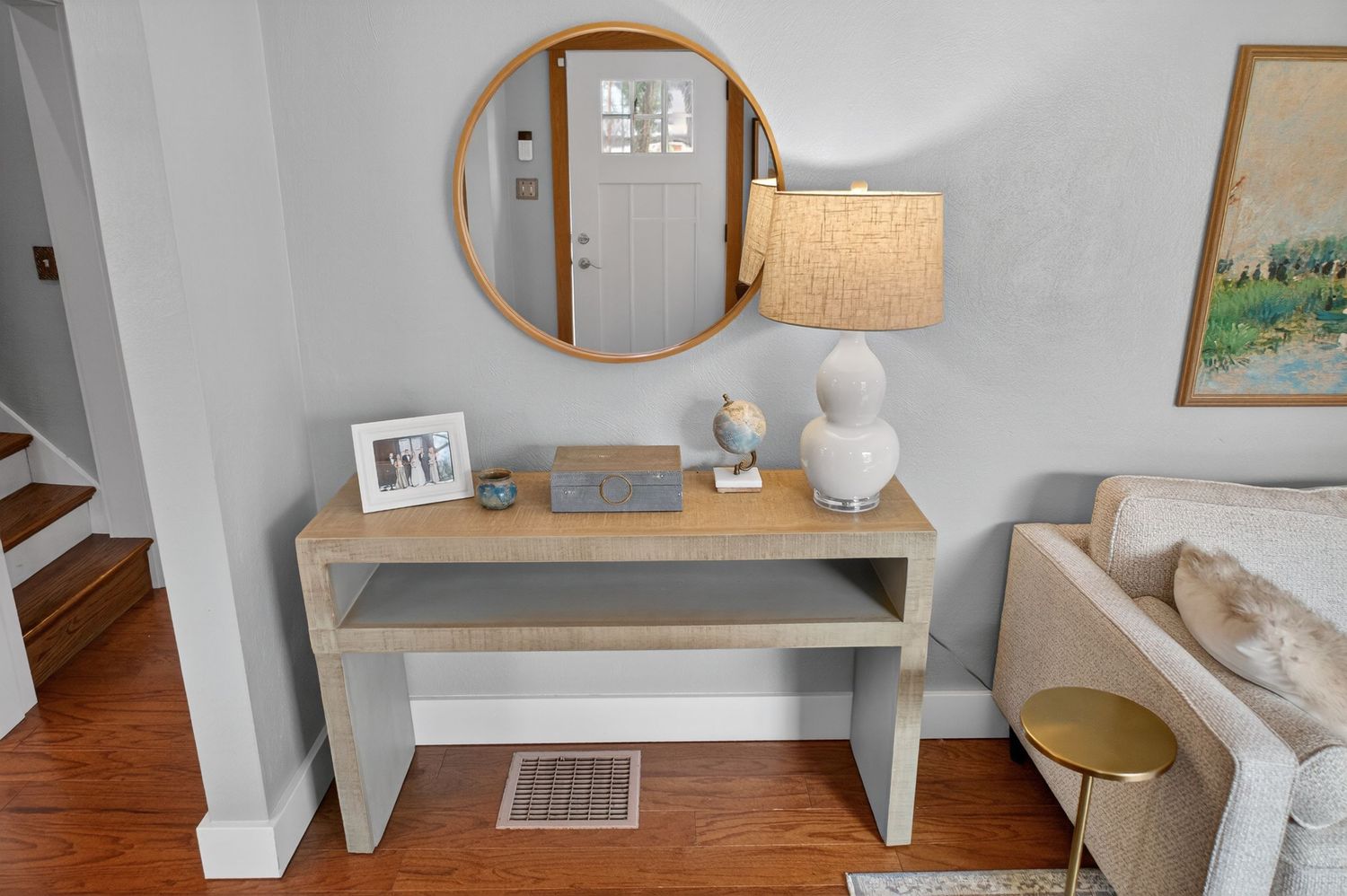 A modern living room features a gray couch, wooden floors, and minimalist decor with white walls and natural lighting.