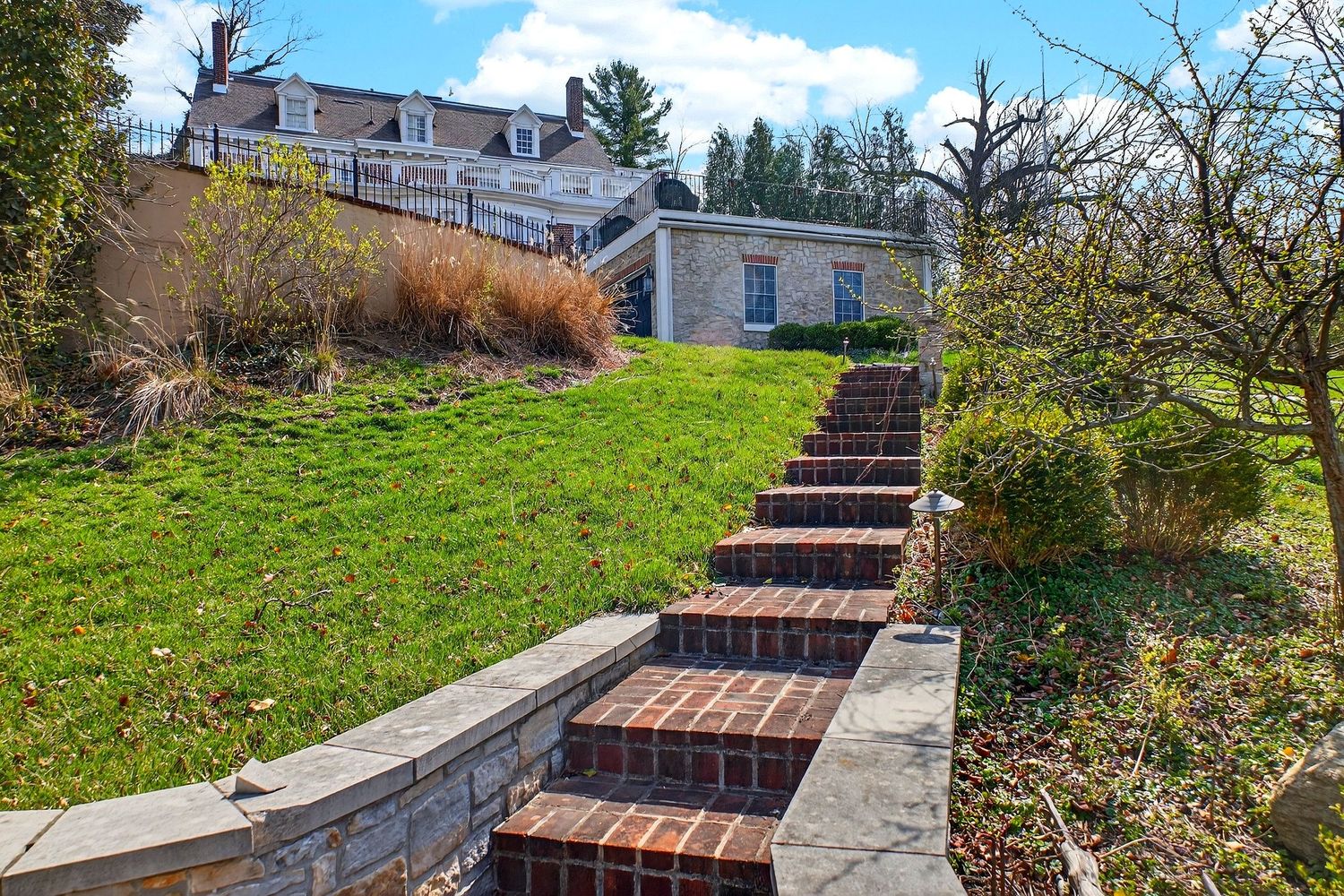 Stone and brick stairway winds up a grassy hillside with concrete retaining walls and landscaping along the path.